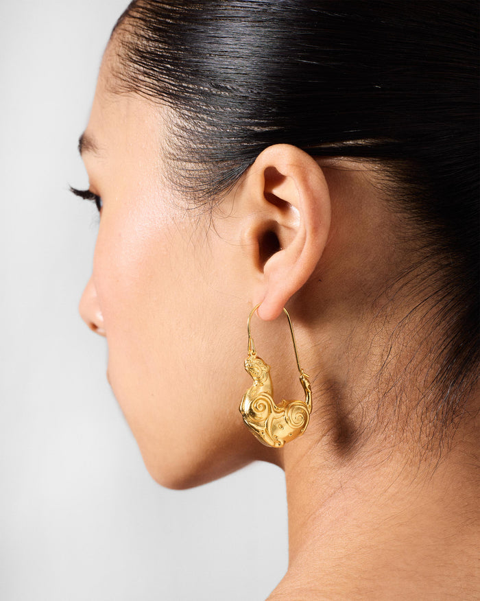 Side profile of a gold leopard hoop earring on a person.