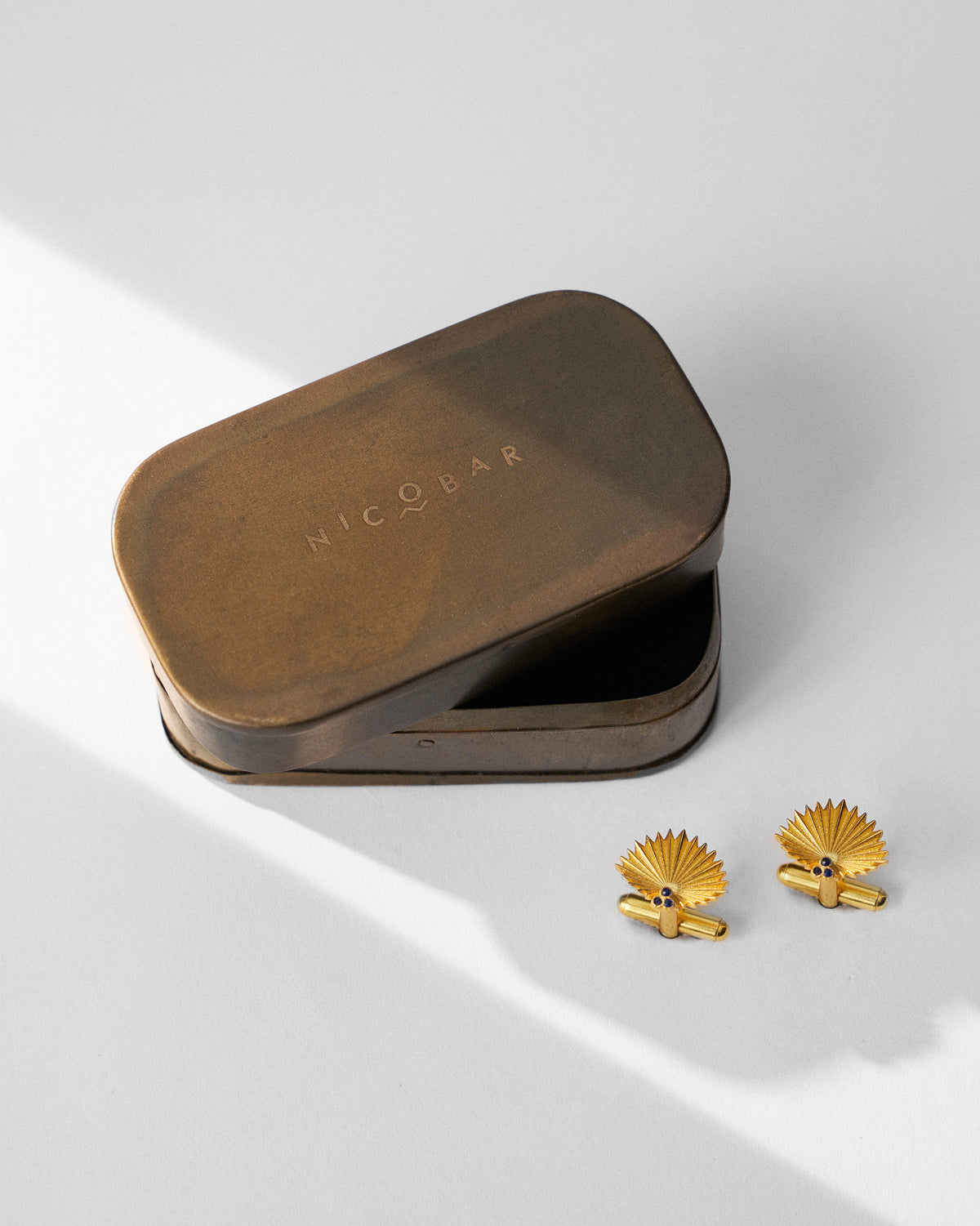 Pair of gold Palm Leaf Cufflinks beside an open brass tin.