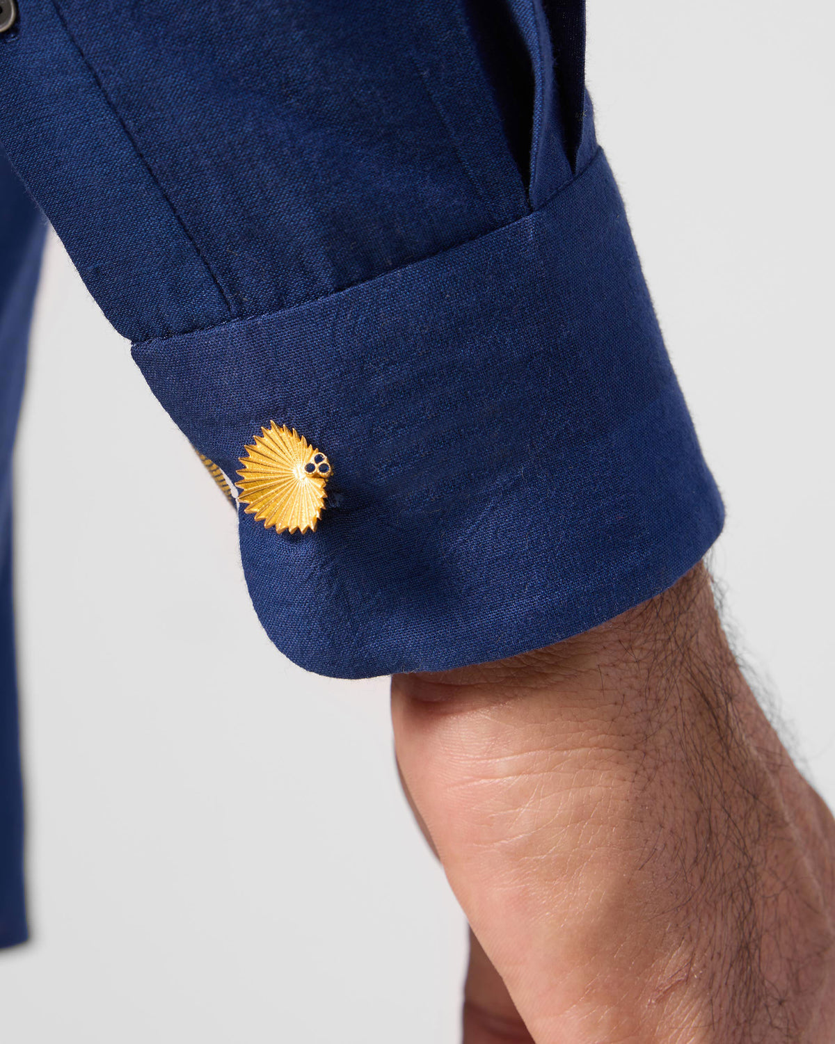 Close-up of a gold Palm Leaf Cufflink fastened on a navy shirt cuff.