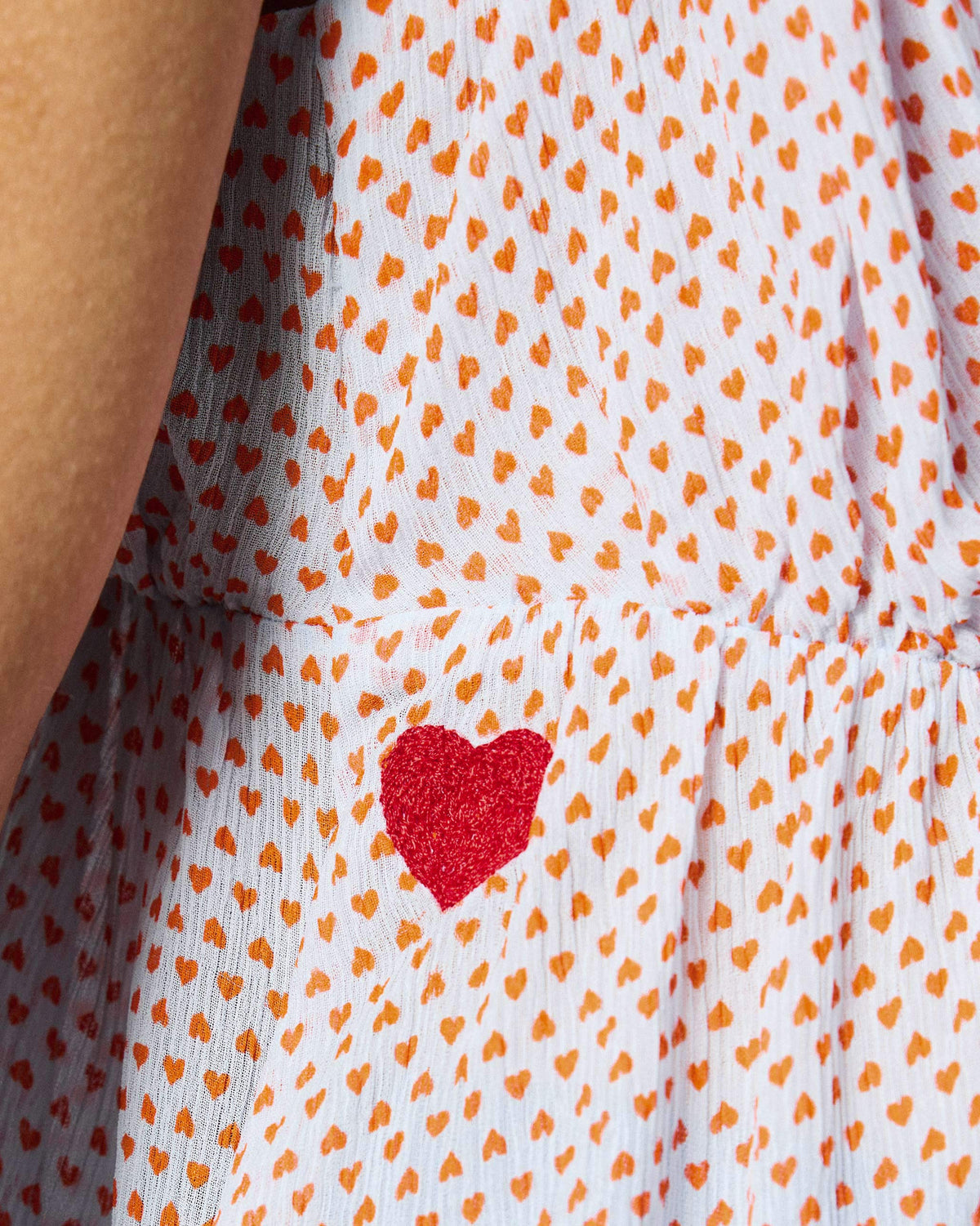 Close-up of a Sira top showing its orange heart print and a red embroidered heart.