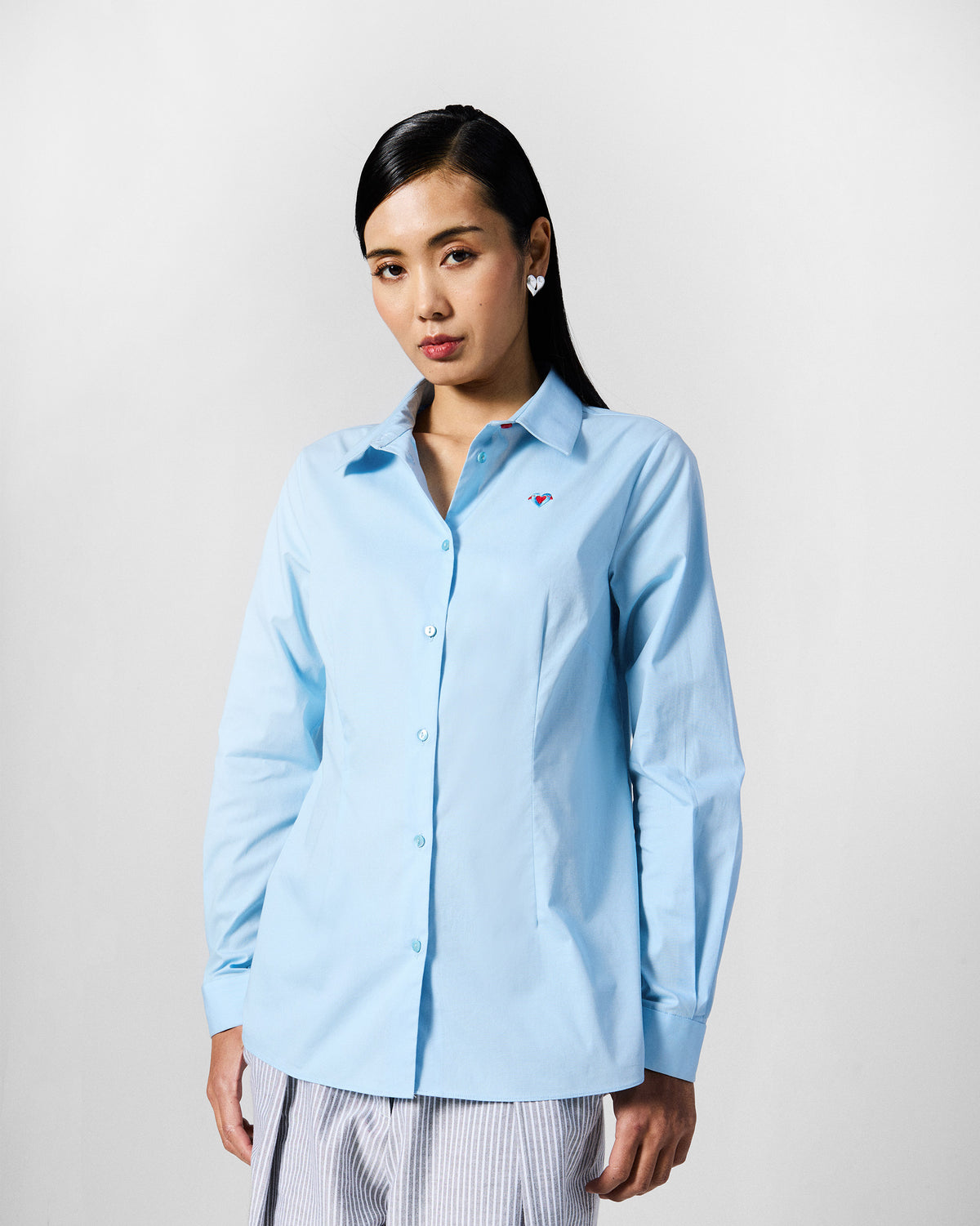 Person wearing an ice blue Ela shirt with a small embroidered chest motif.