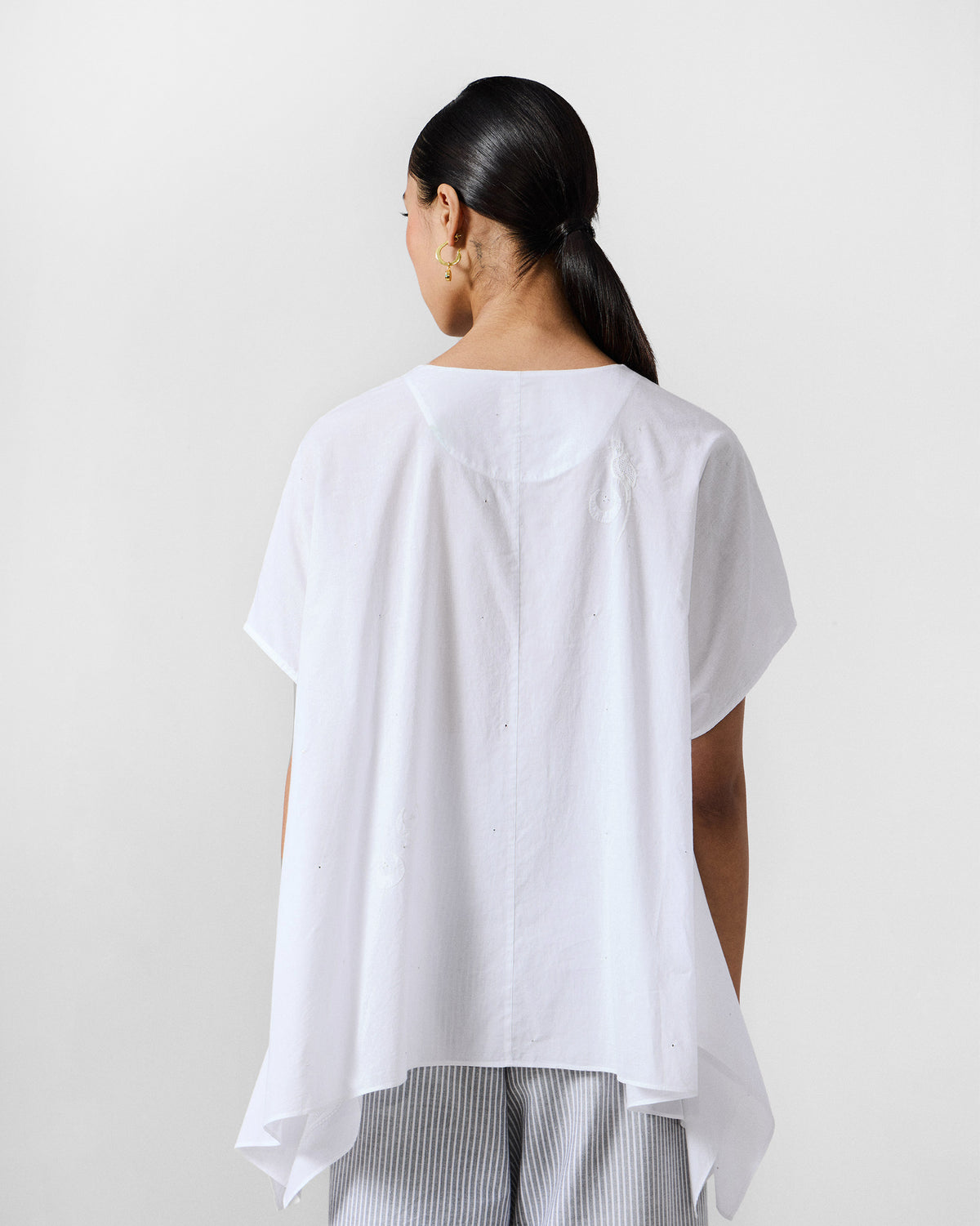 Back of a white oversized top with a flared asymmetrical hem.