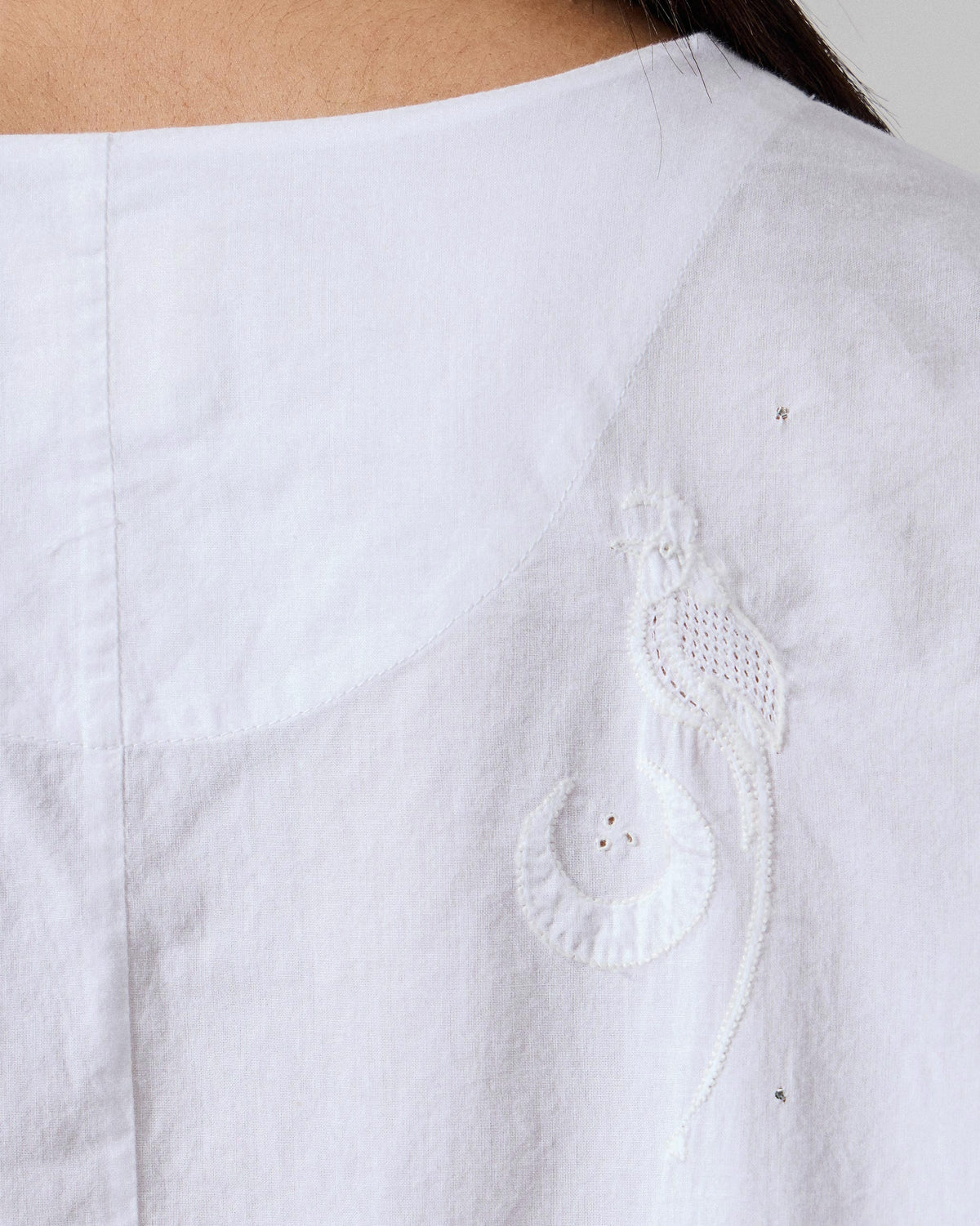 Close-up of a white top with tonal bird embroidery on the back.