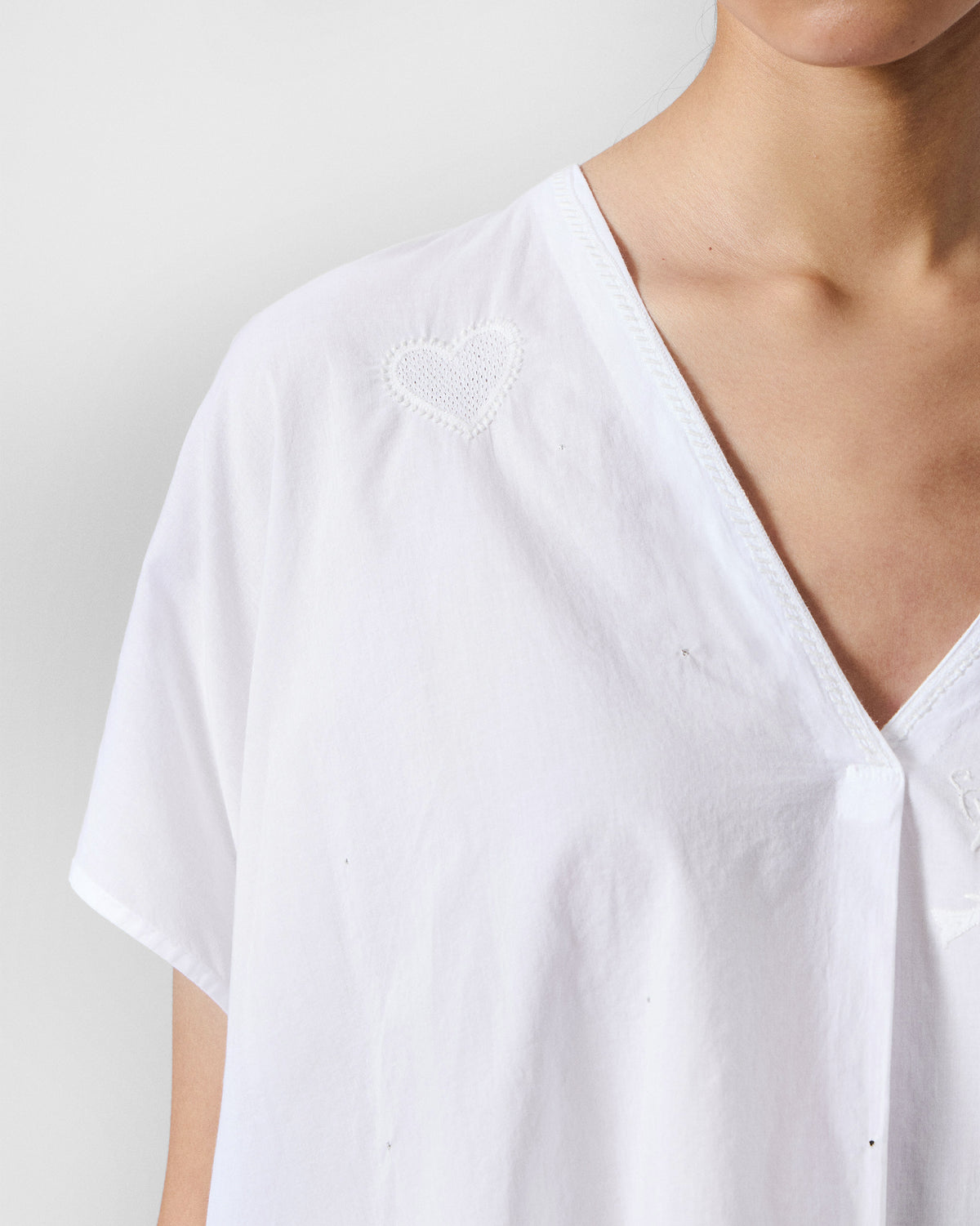 Close-up of a white V-neck top with an embroidered heart.