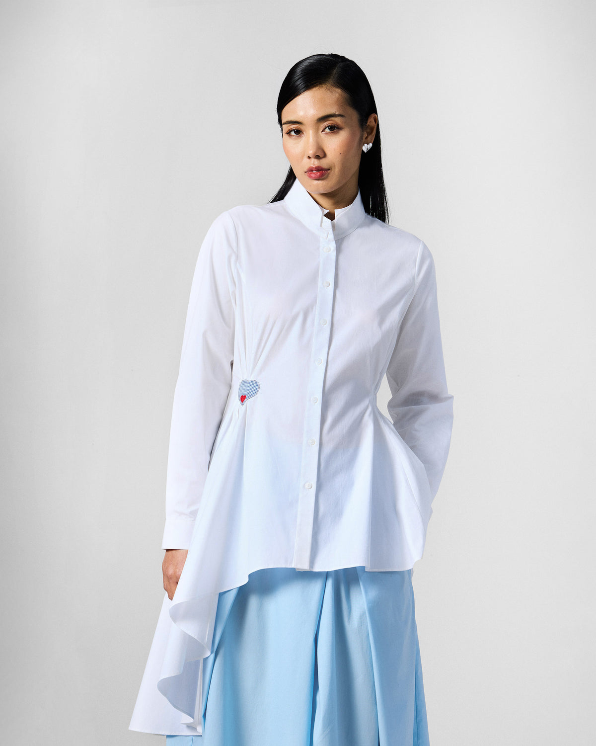 Person wearing a white Rai top with a draped asymmetric hem.