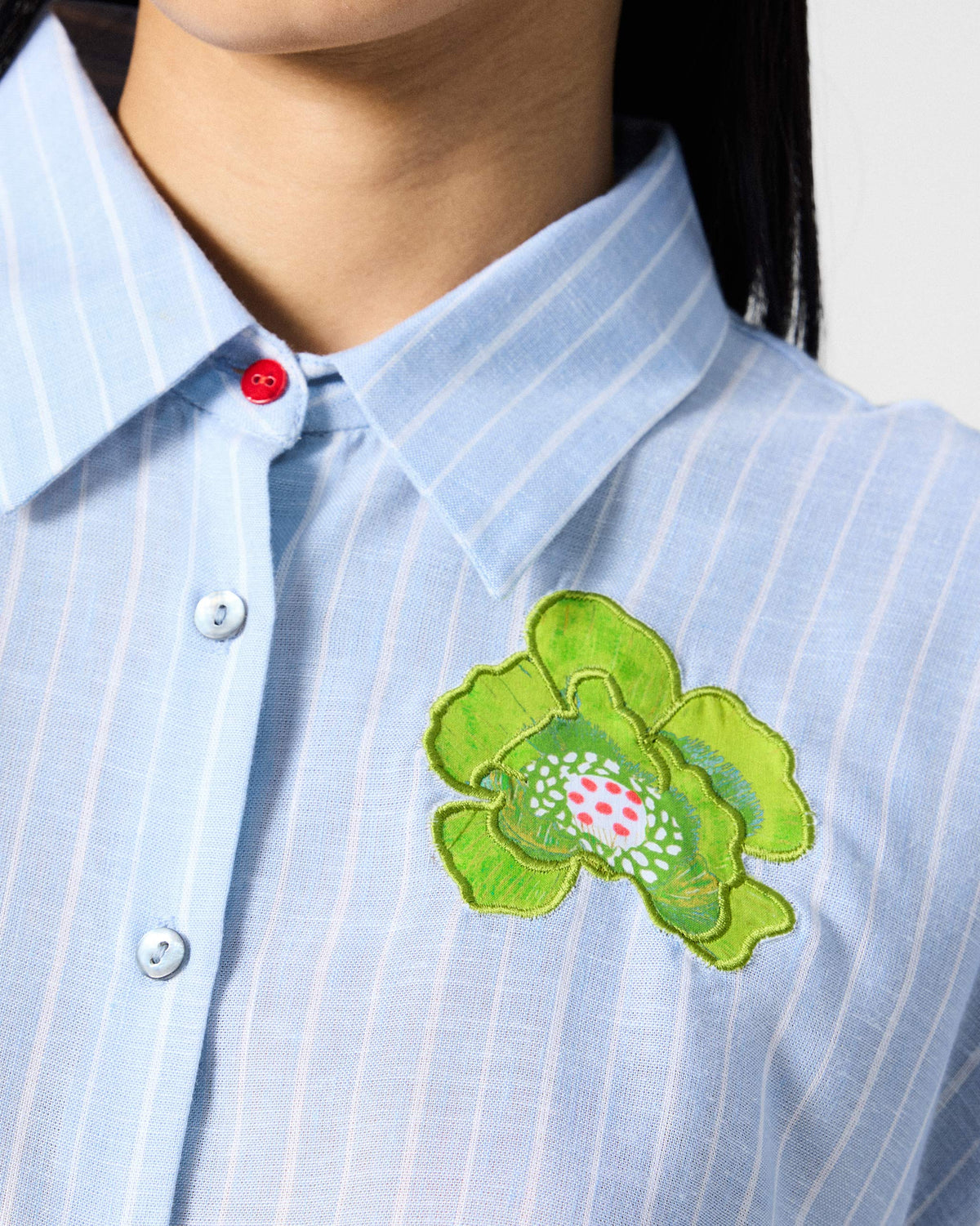Close-up of the lime green flower and red collar button on a blue and white striped Vaah top.