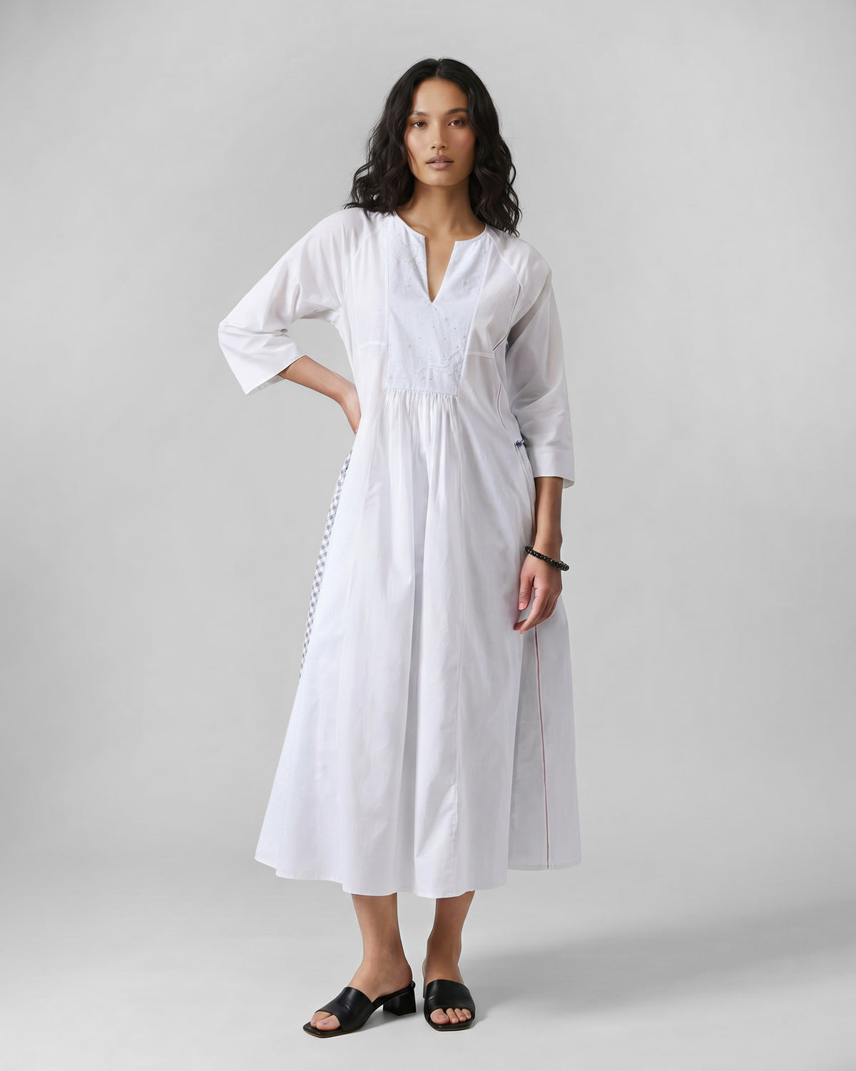 Person wearing a white Torsa dress with embroidery and a blue check side panel.