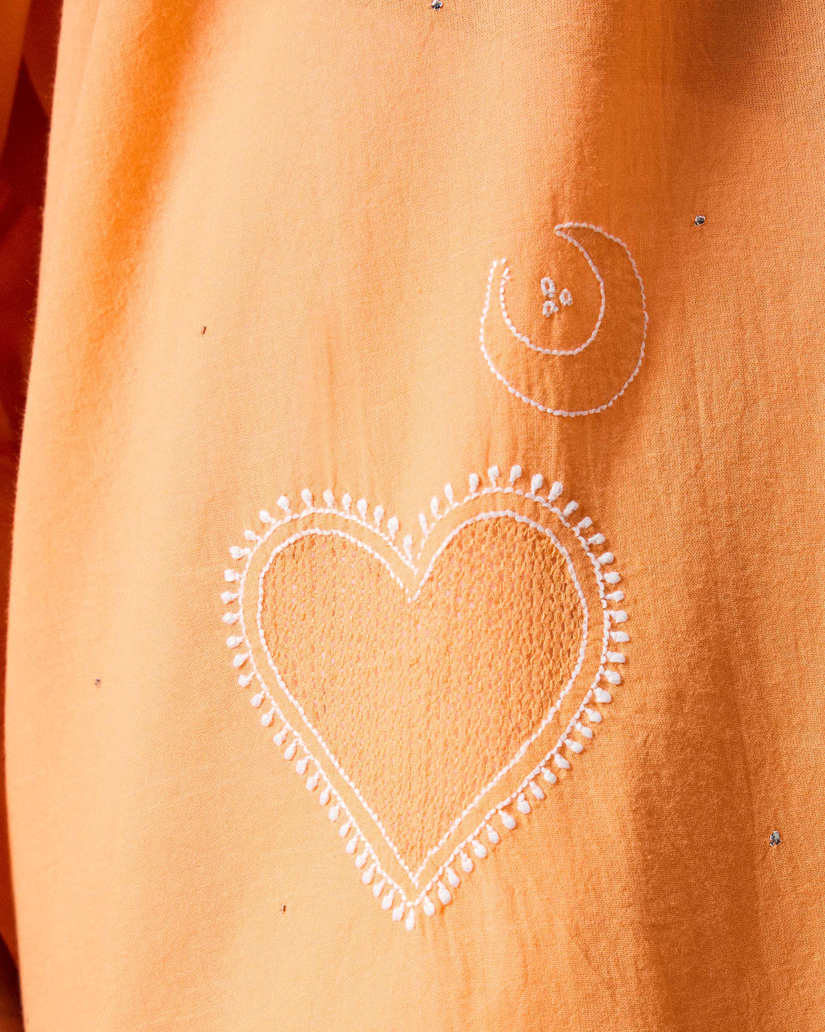Close-up of white heart and moon embroidery on an orange Lazy Sunday tunic.