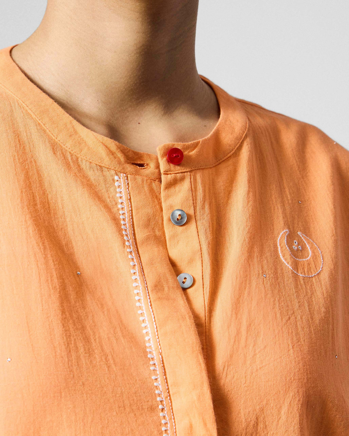Close-up of the band collar and red top button on an orange Lazy Sunday tunic.