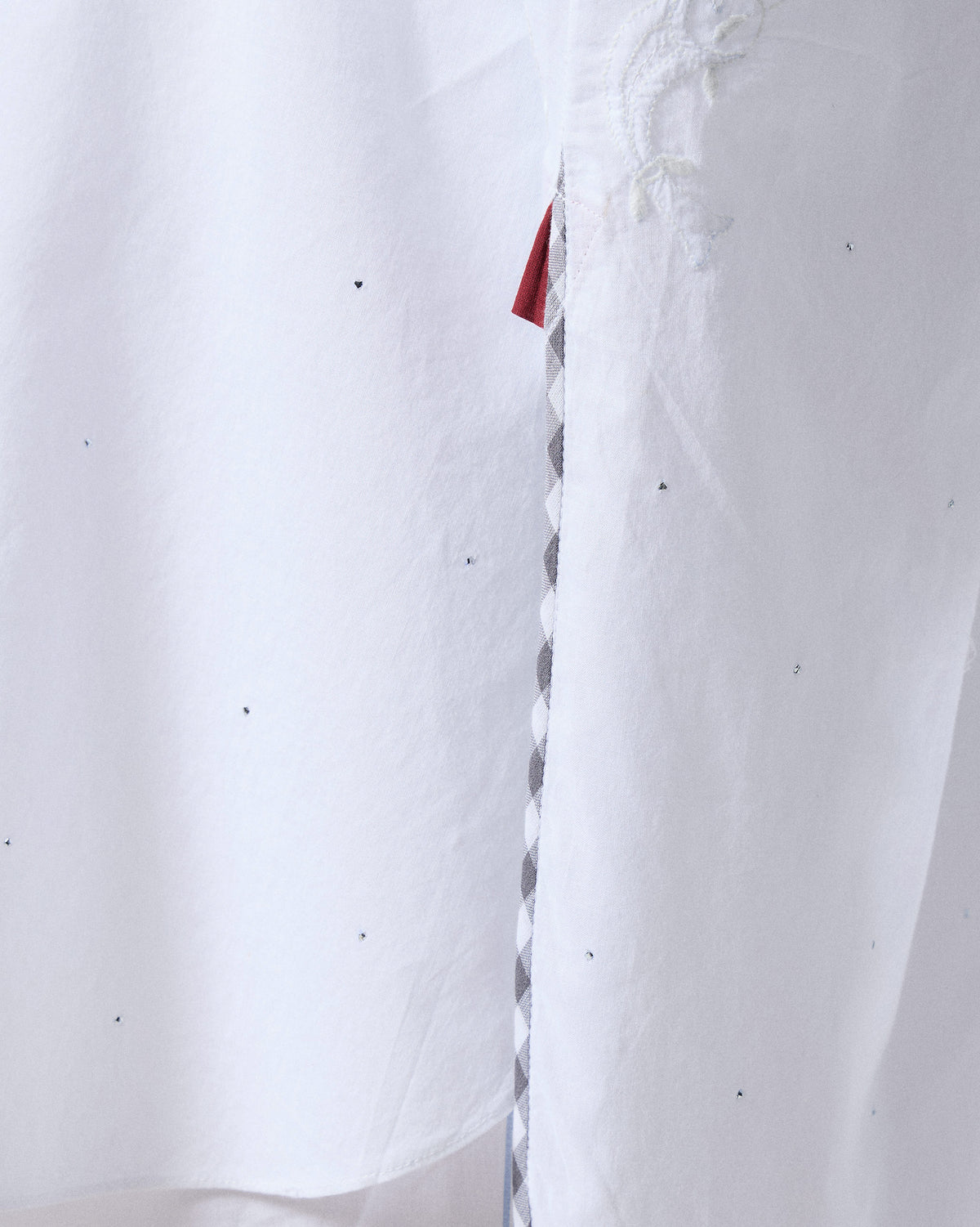 Close-up of gingham piping and a red tab at the side slit of a Calicut kurta.