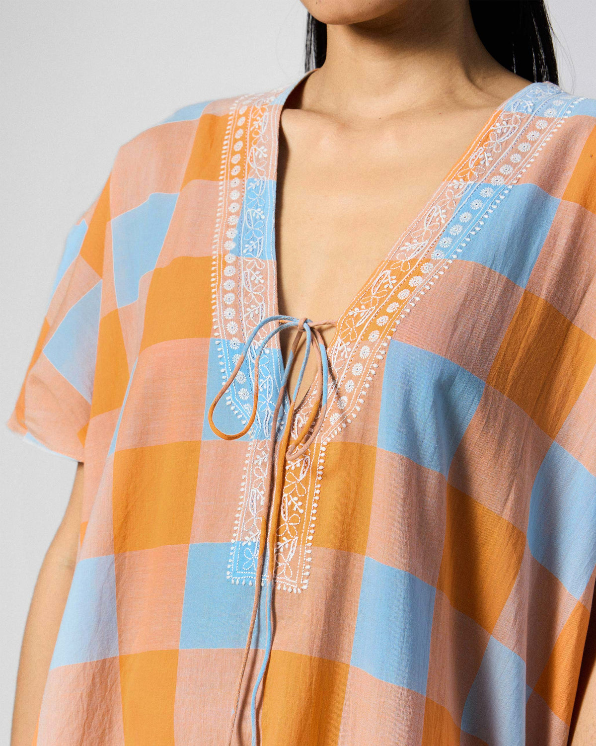 Close-up of a Vaya Kaftan V-neck with white embroidery and drawstring ties.