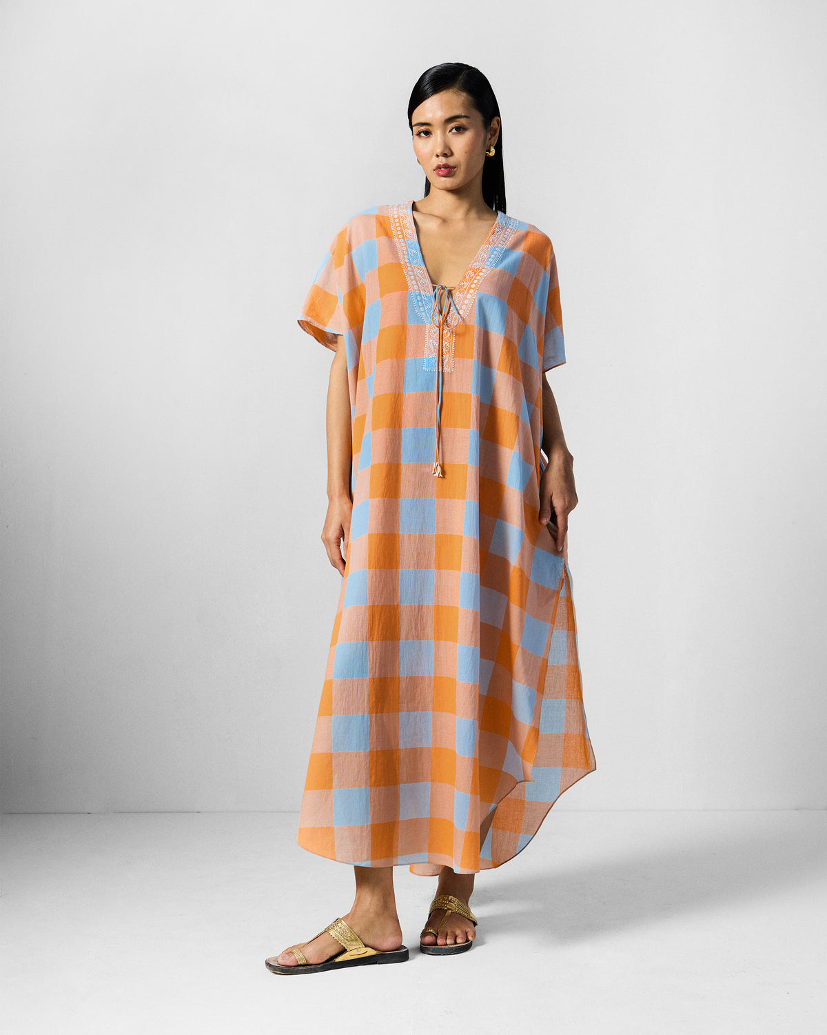 Person wearing a long orange and ice-blue check Vaya Kaftan.