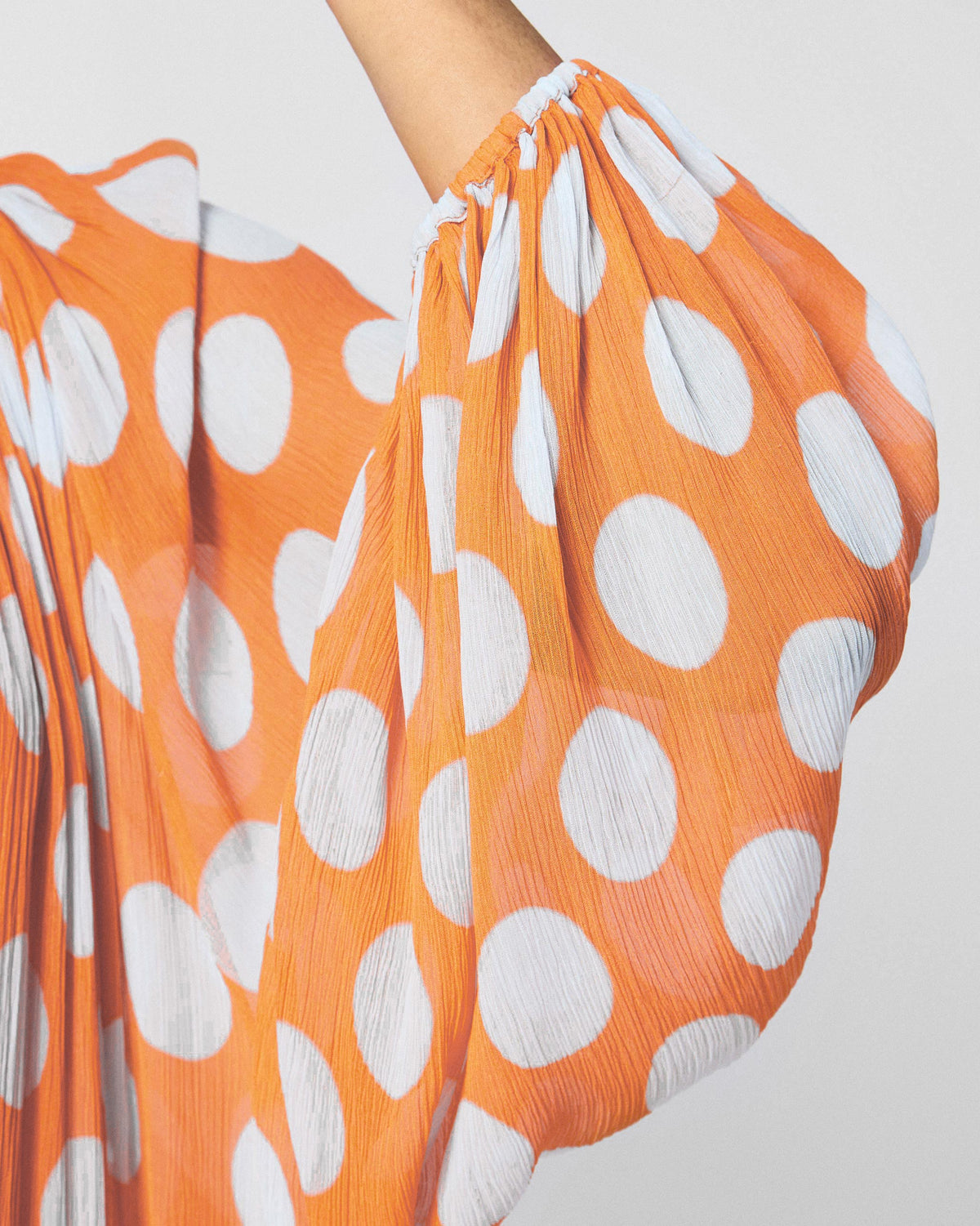Close-up of a gathered sleeve on an orange Sara kaftan with white dots.