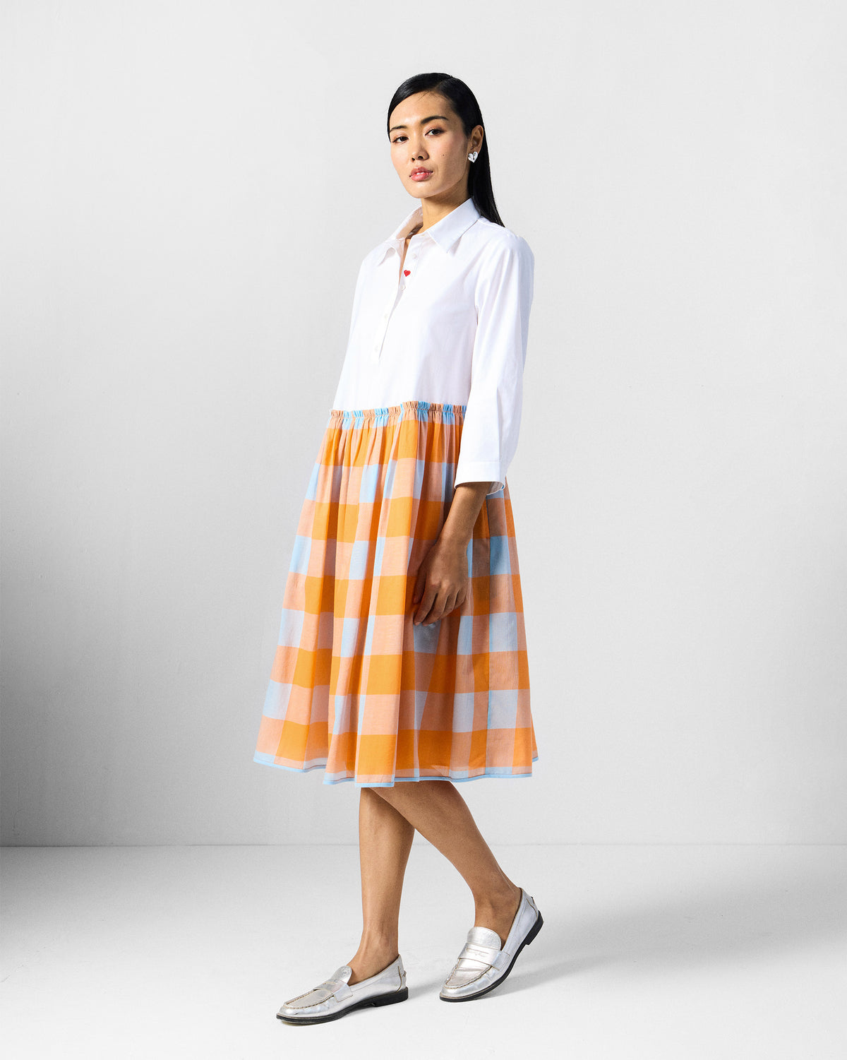 Person wearing a white dress with an orange and blue checked skirt.