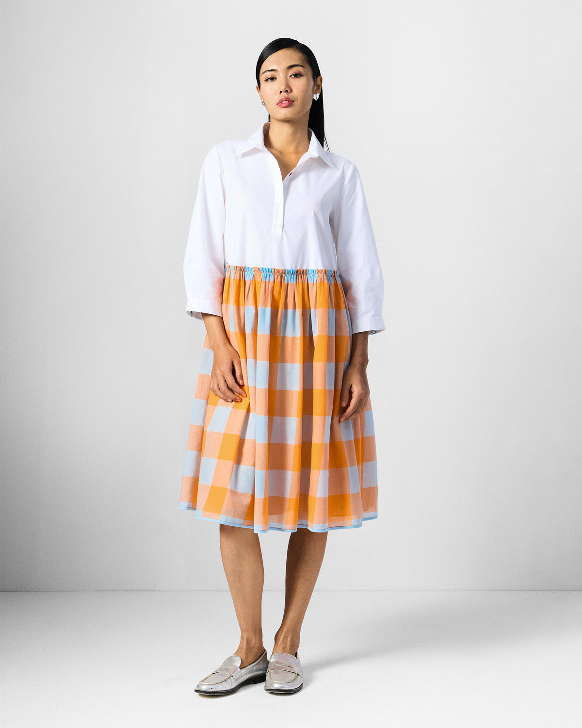Person wearing a white dress with an orange checked skirt.
