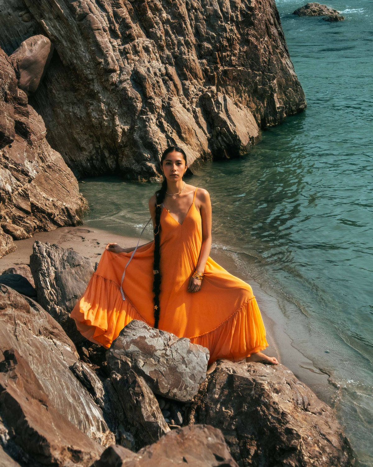 Person wearing an orange Luma dress with thin straps and a tiered skirt.