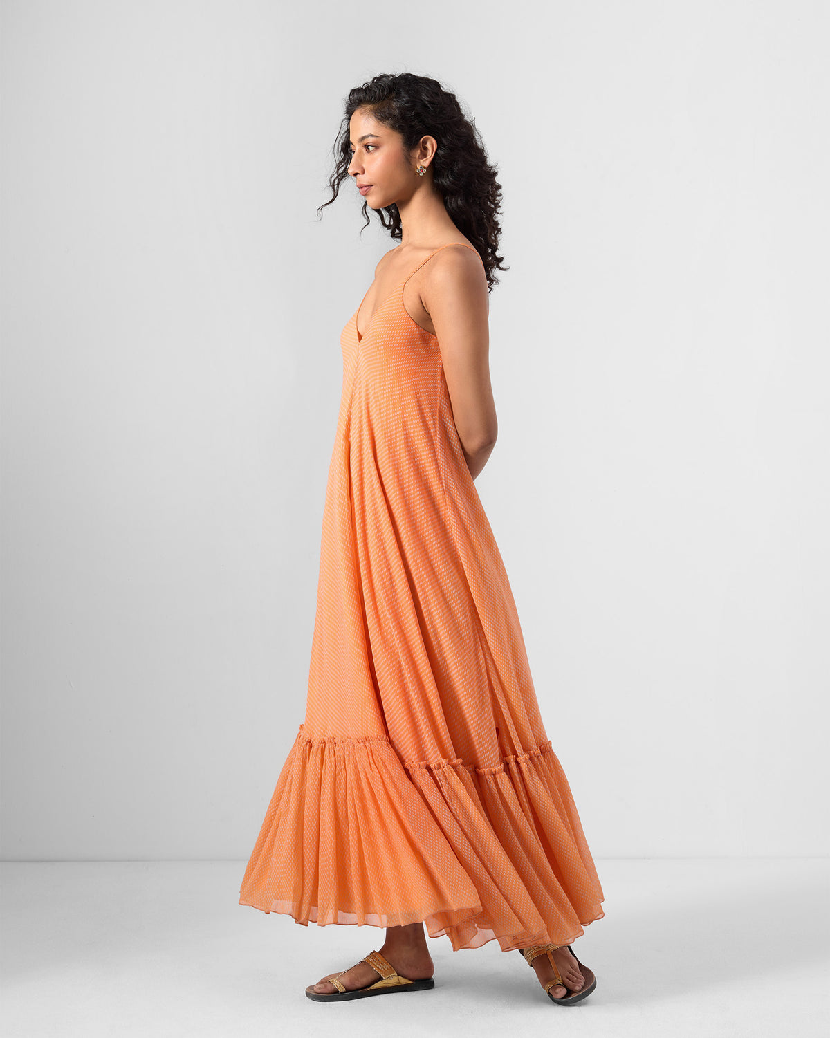 Side view of an orange Luma dress with a flared ruffle hem.