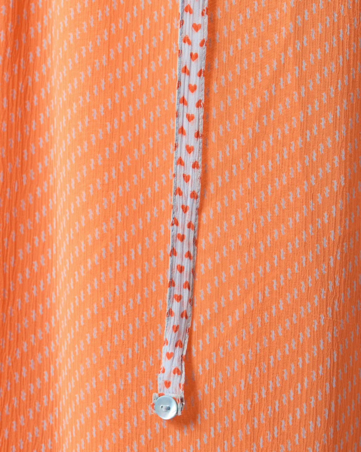 Close-up of orange Luma dress chiffon with a red-heart strap and button.