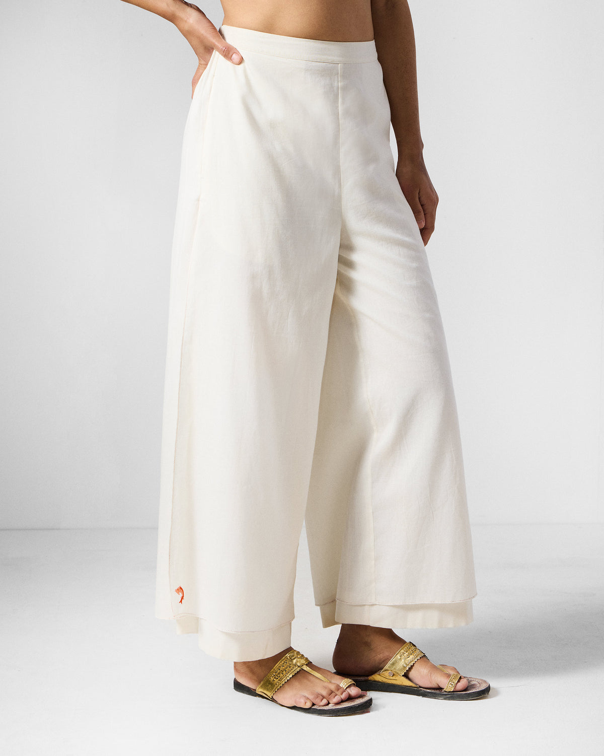 Angled view of ivory Breeze pants with a red palm embroidery at the hem.