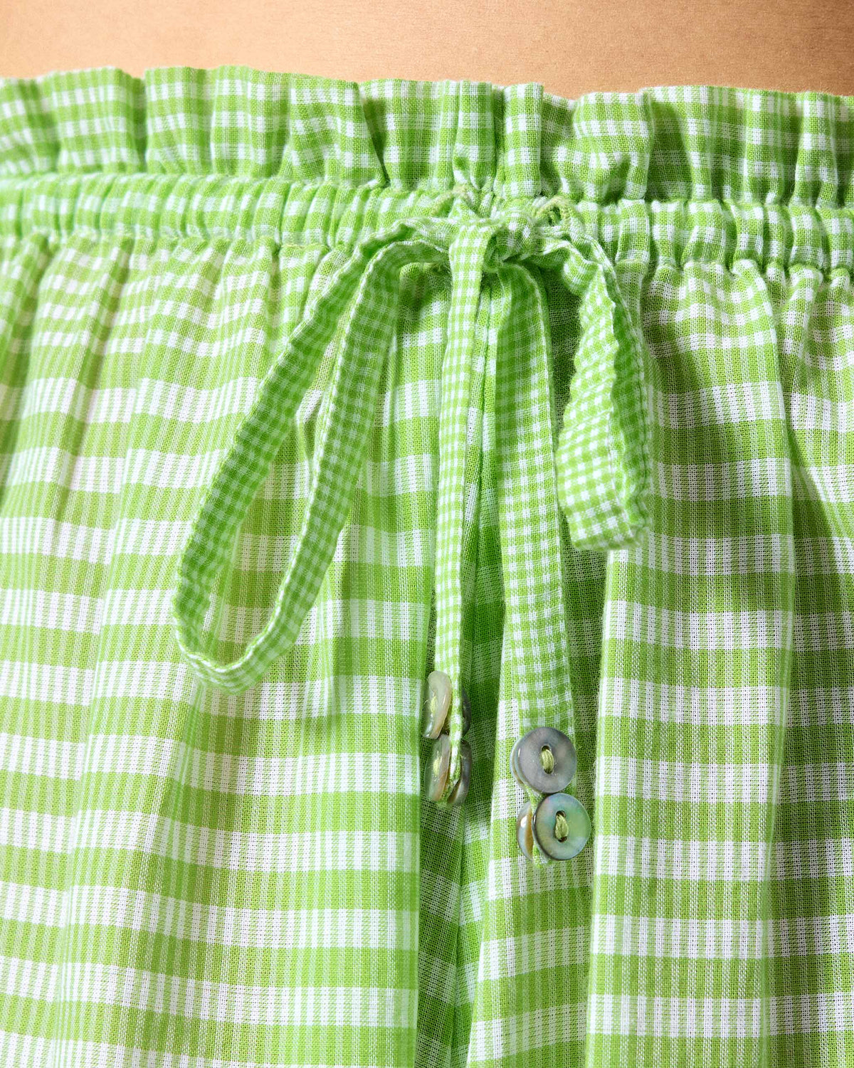 Close-up of light green check Paperbag Pants showing the drawstring waist and shell buttons.