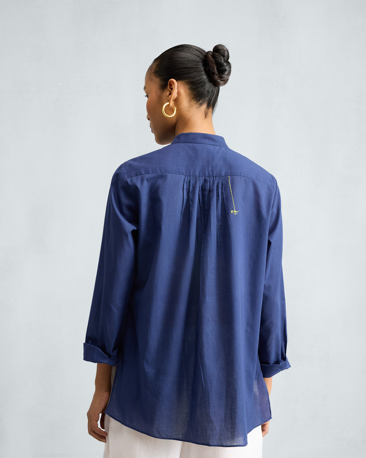 Back of an ink blue mandarin collar top with a gathered yoke and green bird.