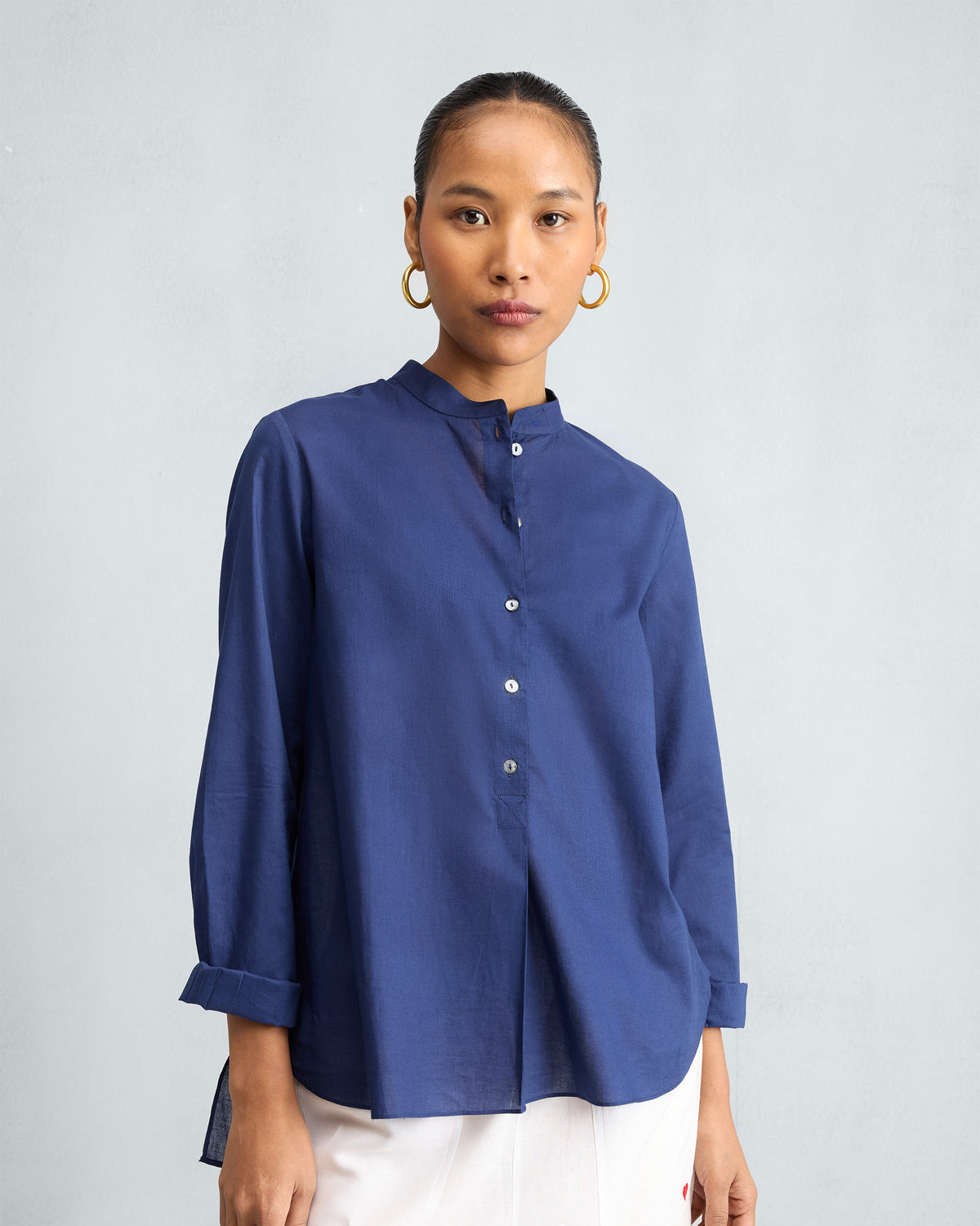 Person wearing an ink blue mandarin collar top with rolled sleeves.