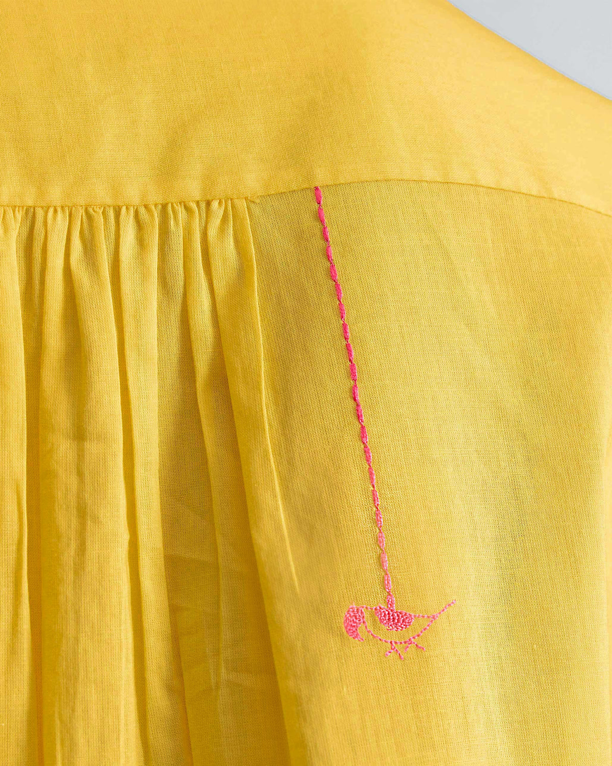 Close-up of a pink parrot on a yellow mandarin collar top.