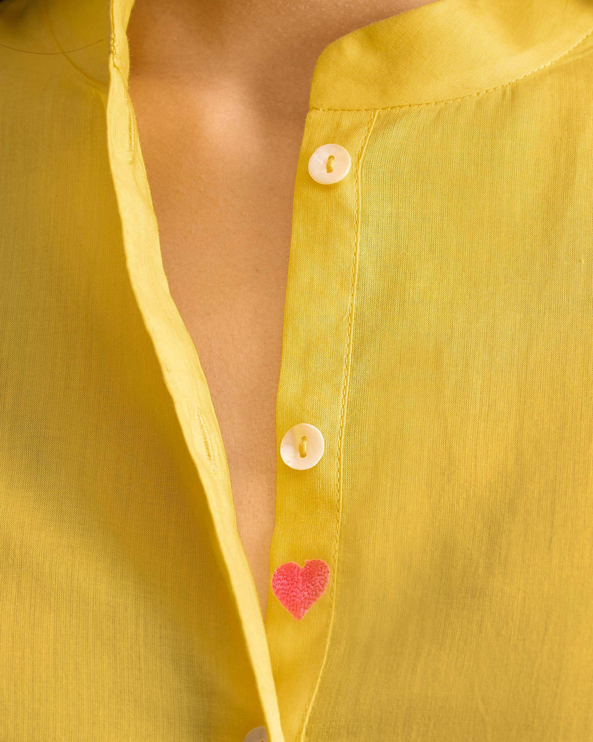 Close-up of a pink heart on a yellow mandarin collar top.