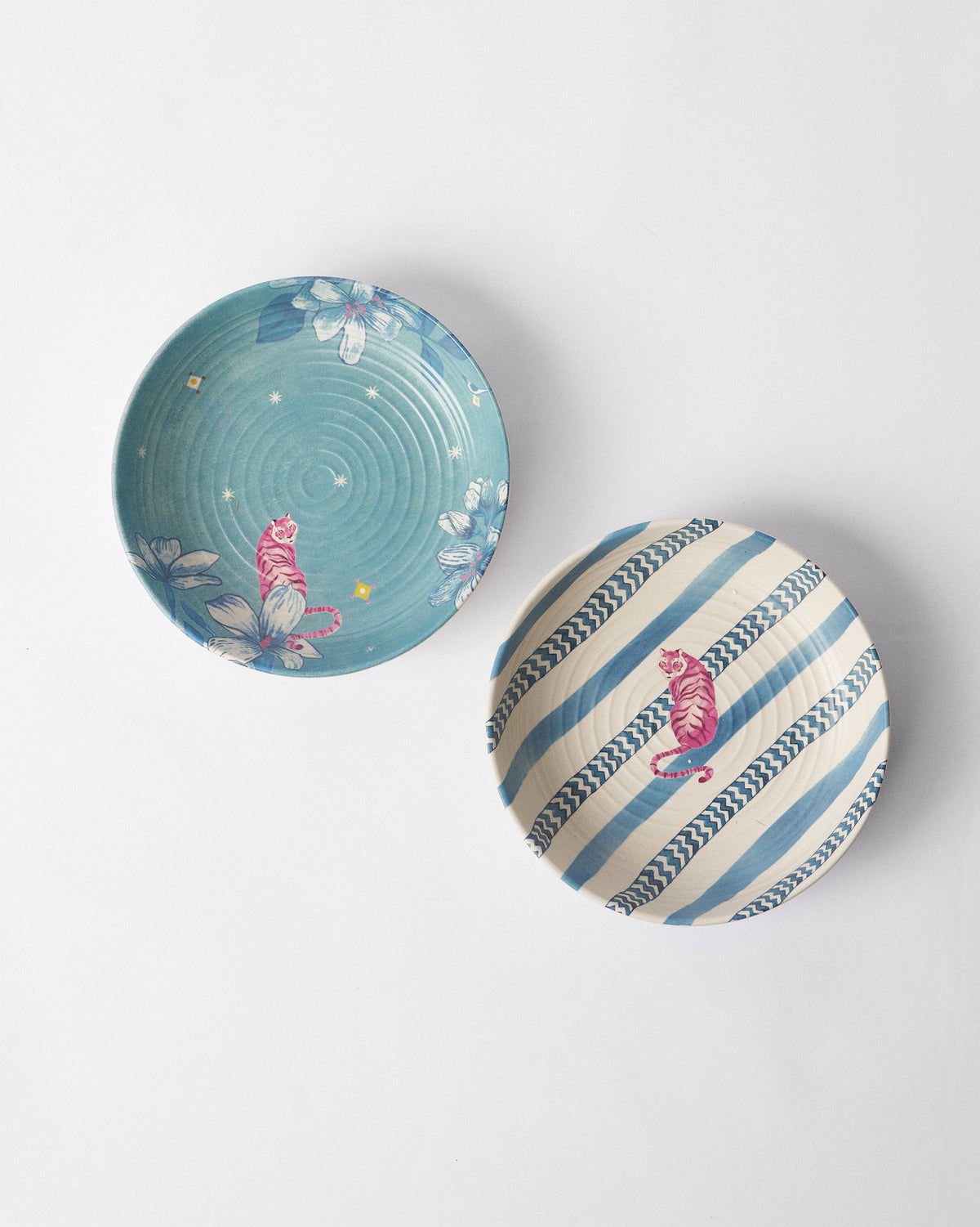 Two River Tiger shallow bowls with pink tiger motifs on teal floral and blue striped interiors.
