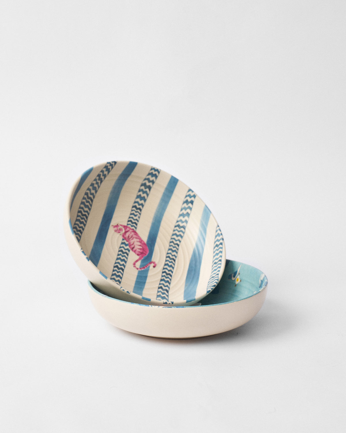 Stacked River Tiger shallow bowls showing a pink tiger on a blue striped interior.
