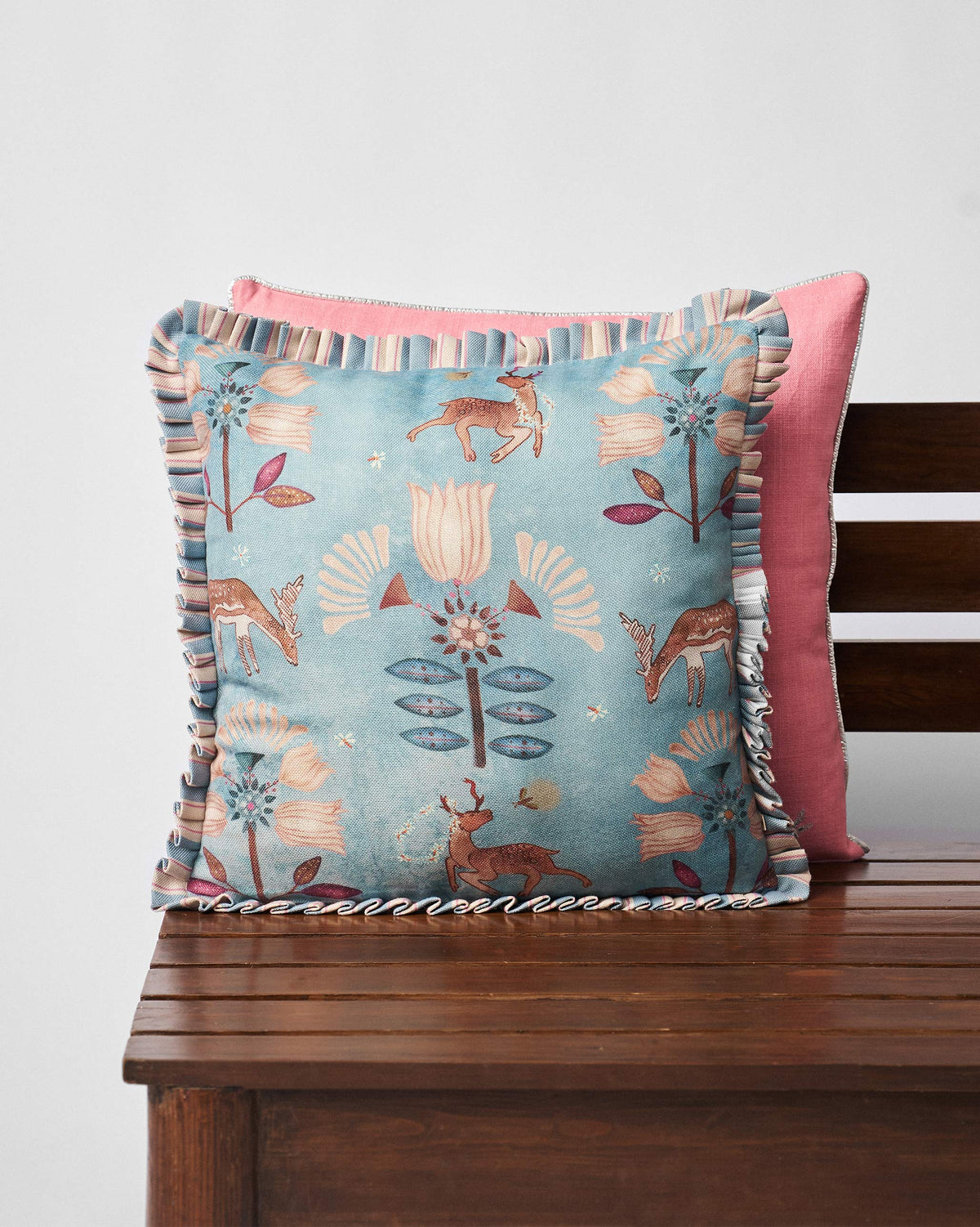 Deer Dance Cushion Cover in blue with deer and flower motifs and a striped frill edge.