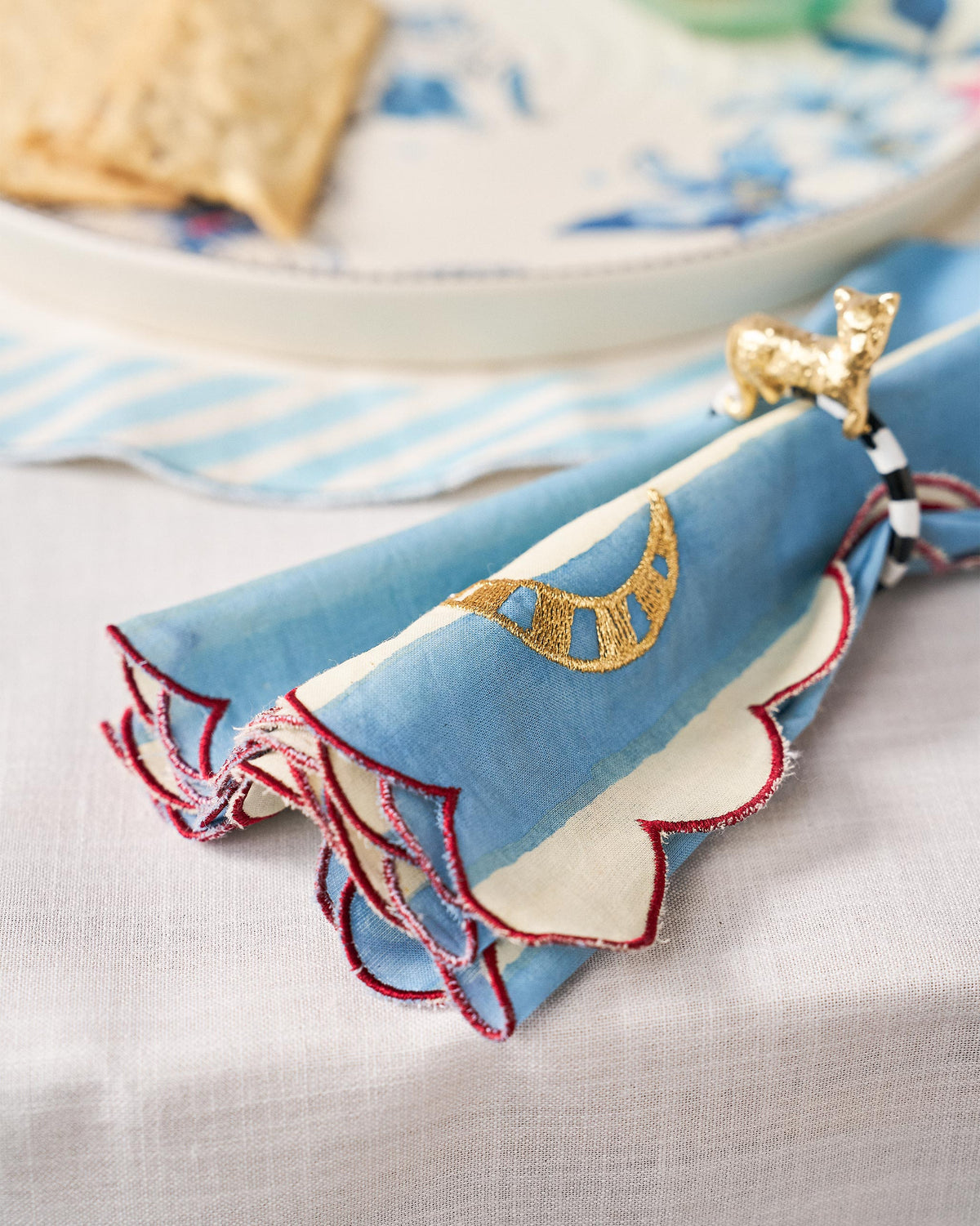 Blue-and-cream striped napkin with a red scalloped edge and gold moon motif.