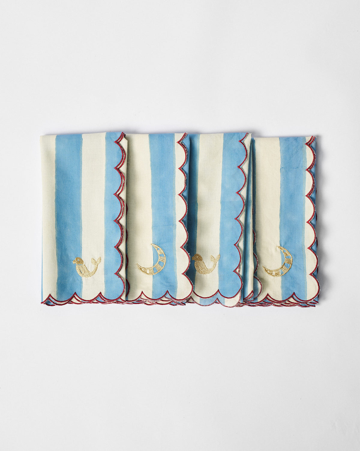 Four folded river-stripe napkins with gold bird and crescent moon embroidery.