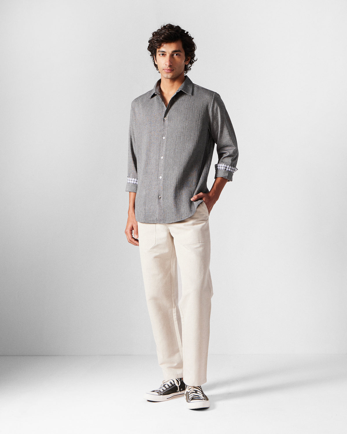 Person wearing a charcoal Nava shirt with rolled sleeves and gingham-lined cuffs.