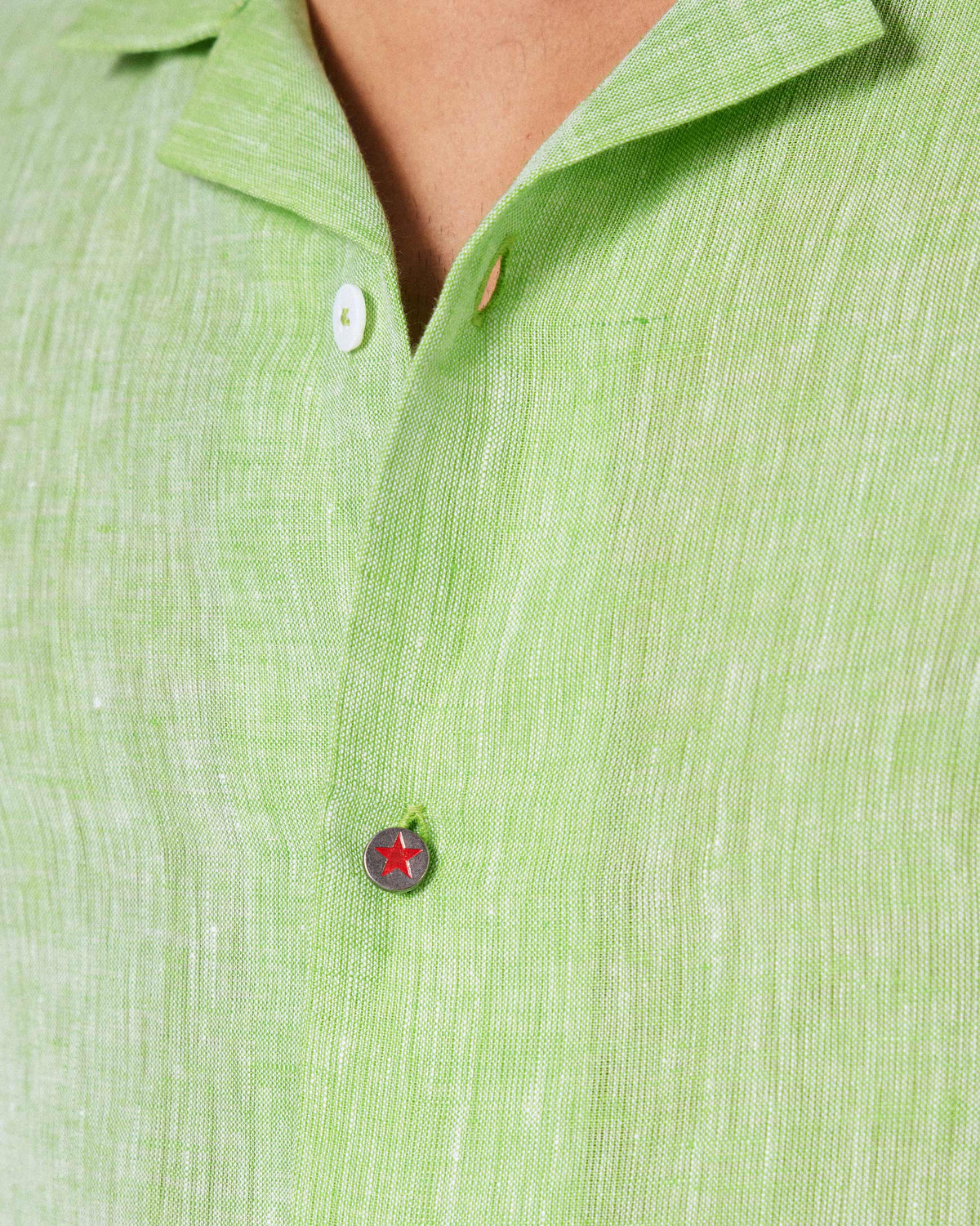 Close-up of a red star button on a light green Mistari shirt.