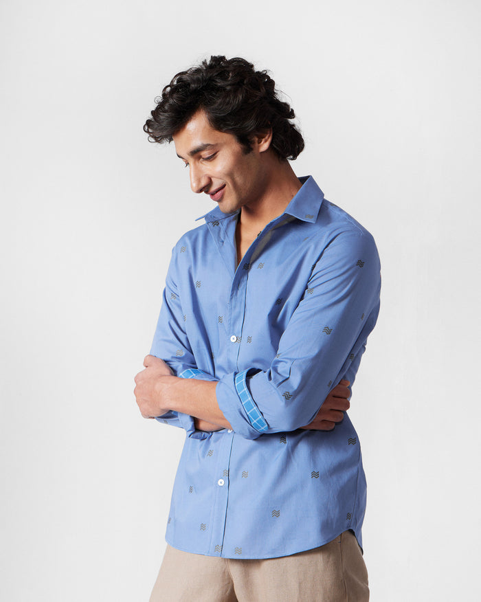 Person wearing a blue Sindhu Shirt with rolled sleeves and a check cuff lining.