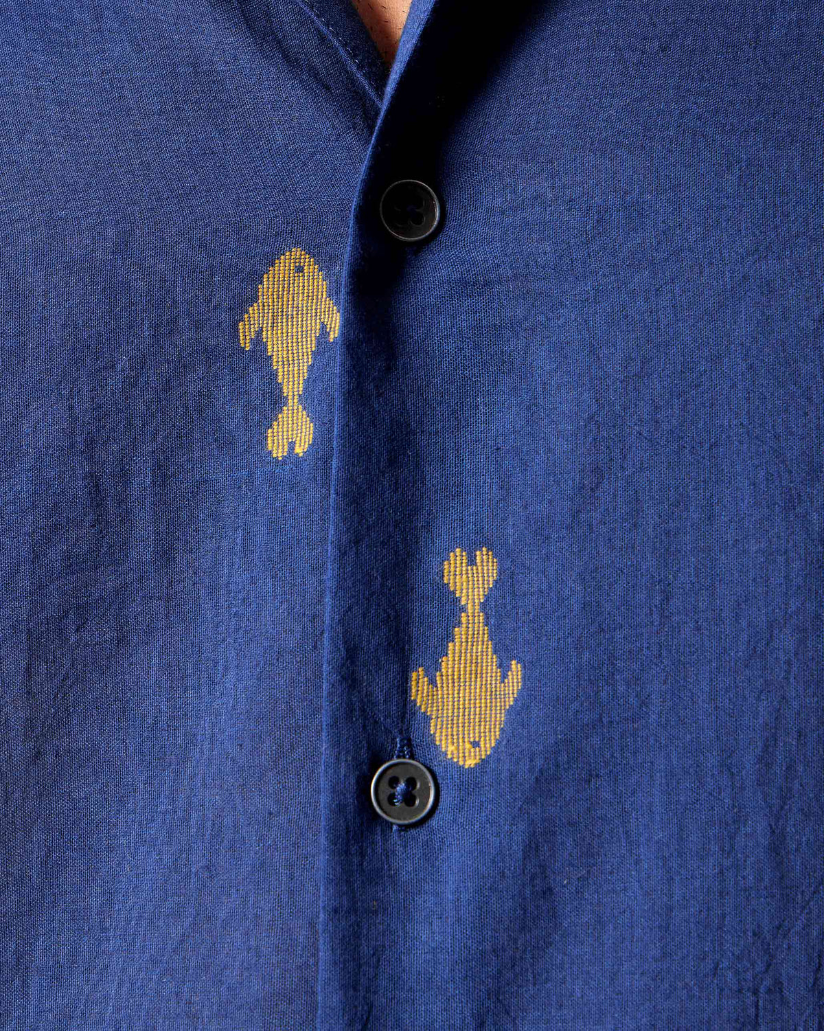 Close-up of yellow fish embroidery on a navy Hakuna Shirt.