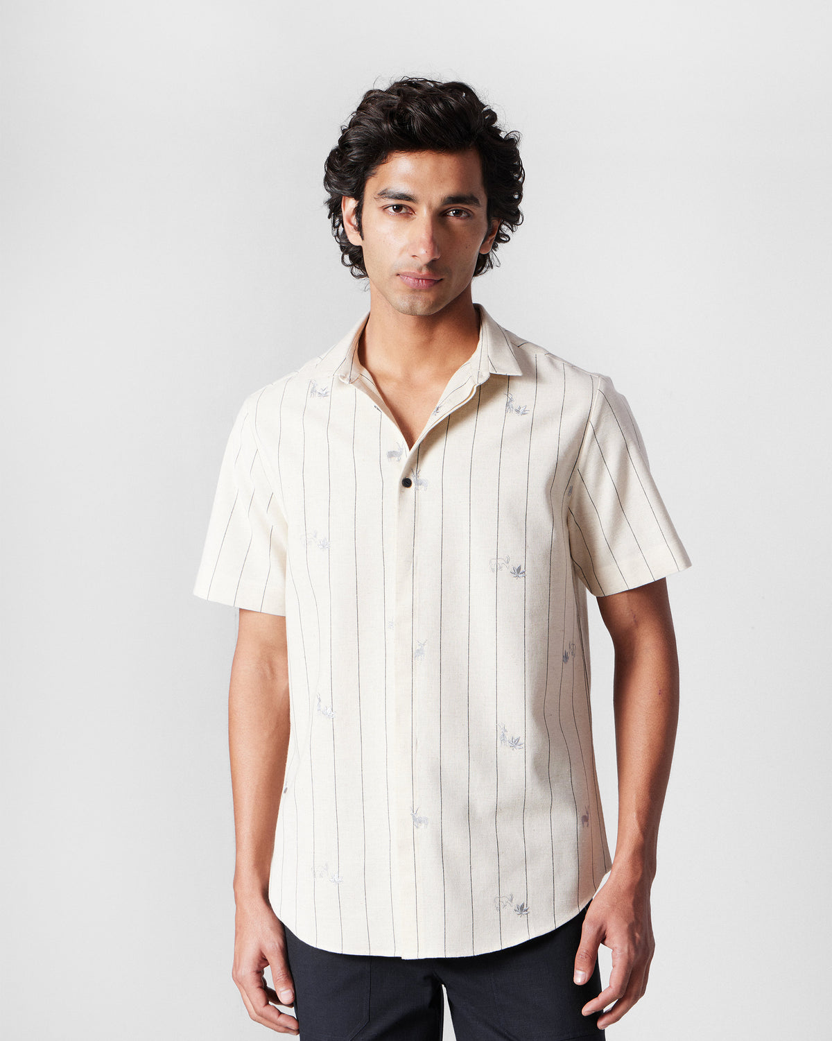 Person wearing an ivory Riverine Shirt with charcoal stripes and embroidered motifs.