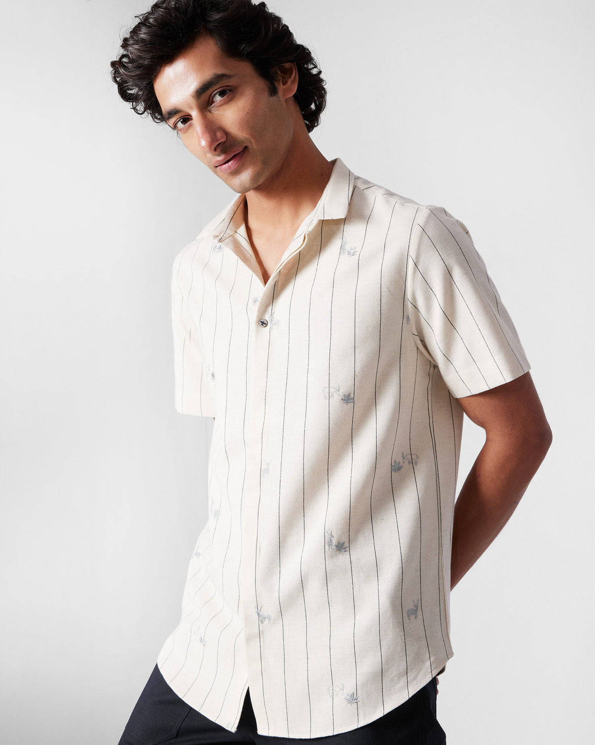 Person wearing an ivory Riverine Shirt with charcoal stripes and embroidered motifs.