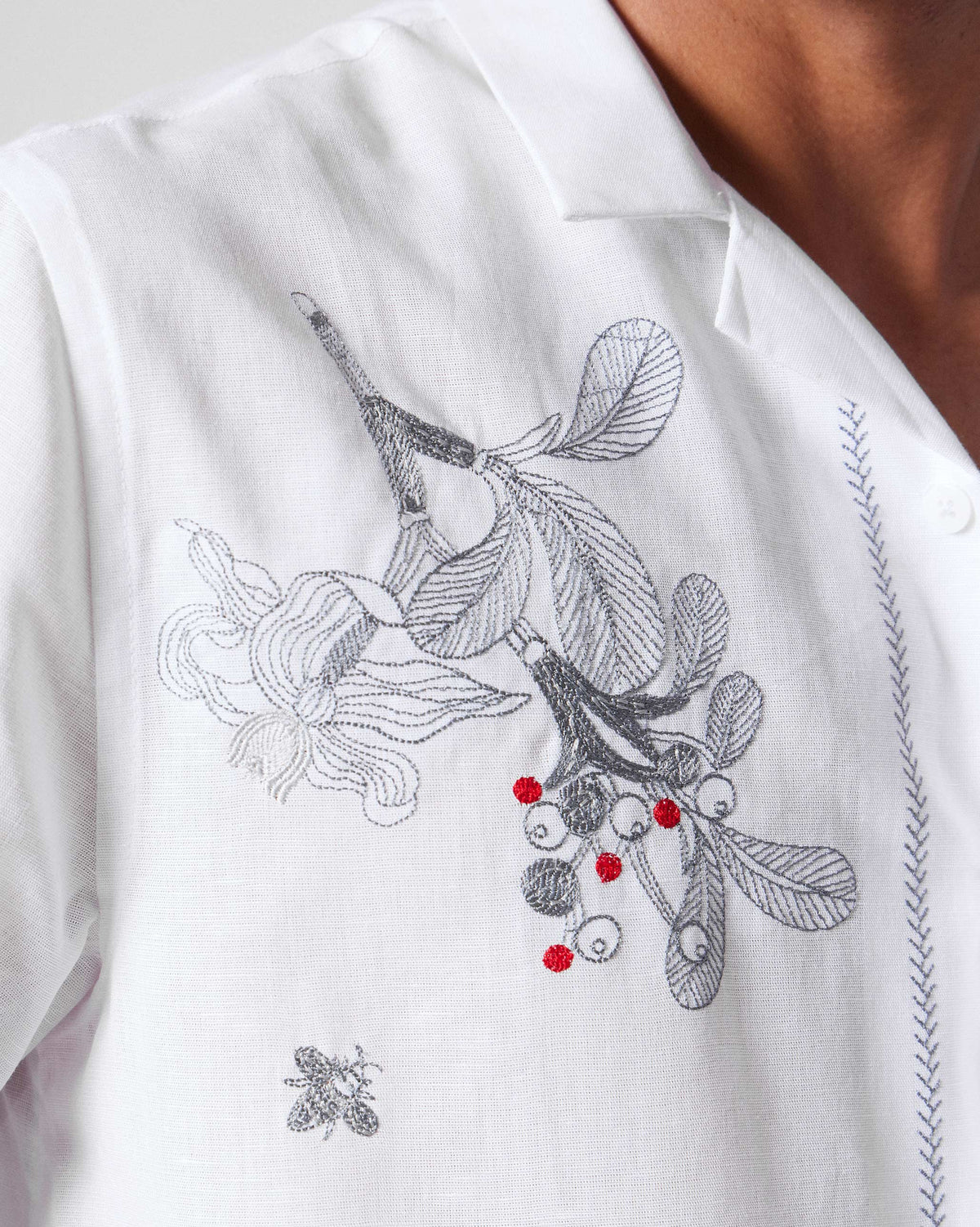 Close-up of a white Delta shirt showing floral embroidery with red berries and a bee.