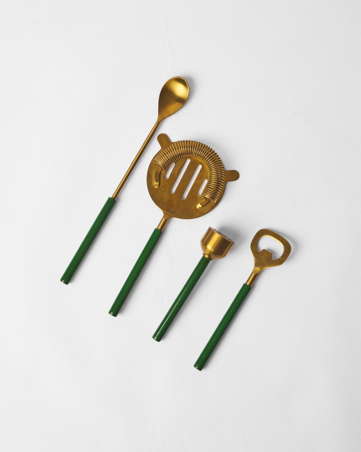 Gold Bash bar spoon, strainer, jigger, and bottle opener with green handles.