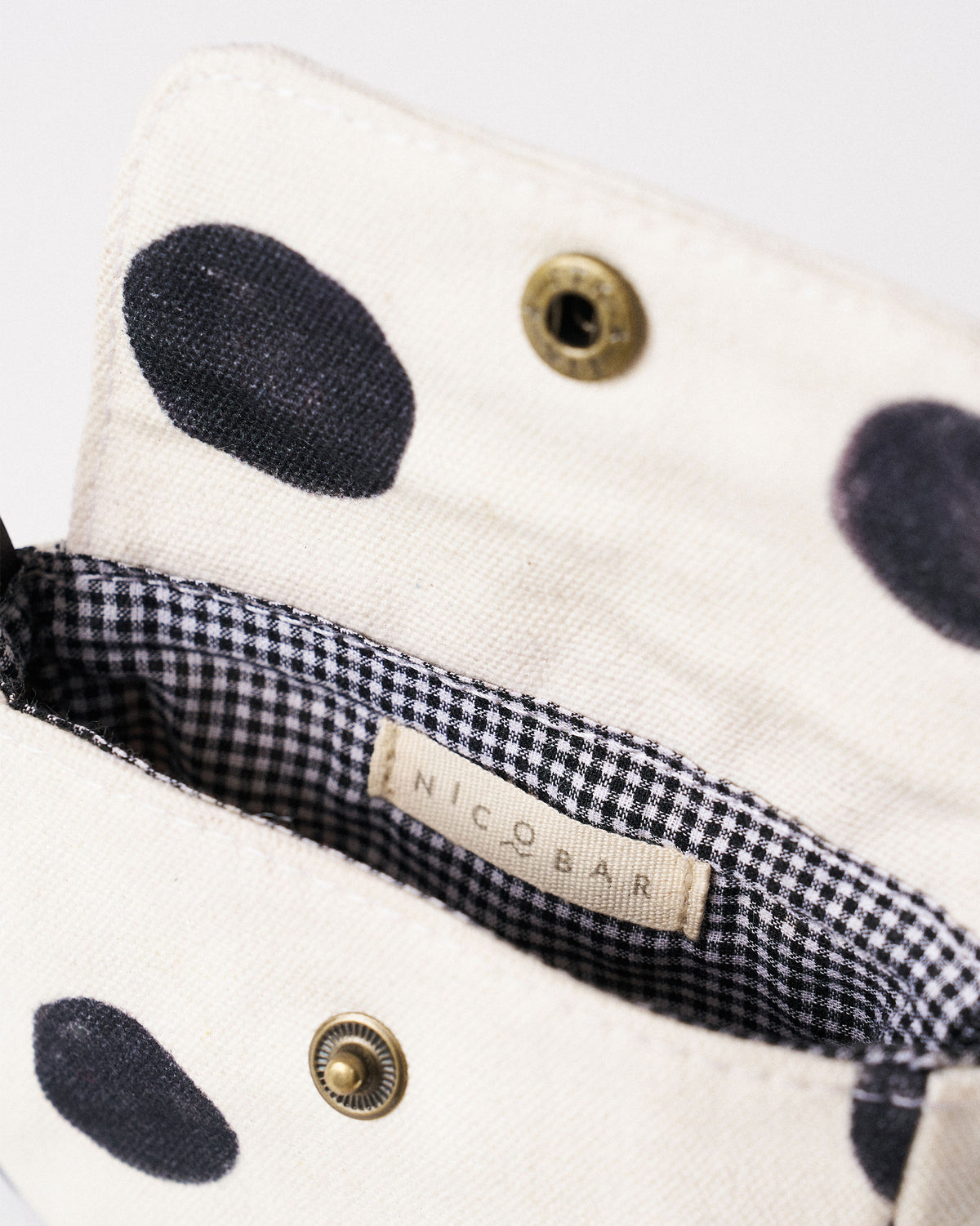 Interior of an ivory Polka Coin Pouch with gingham lining and a Nicobar label.