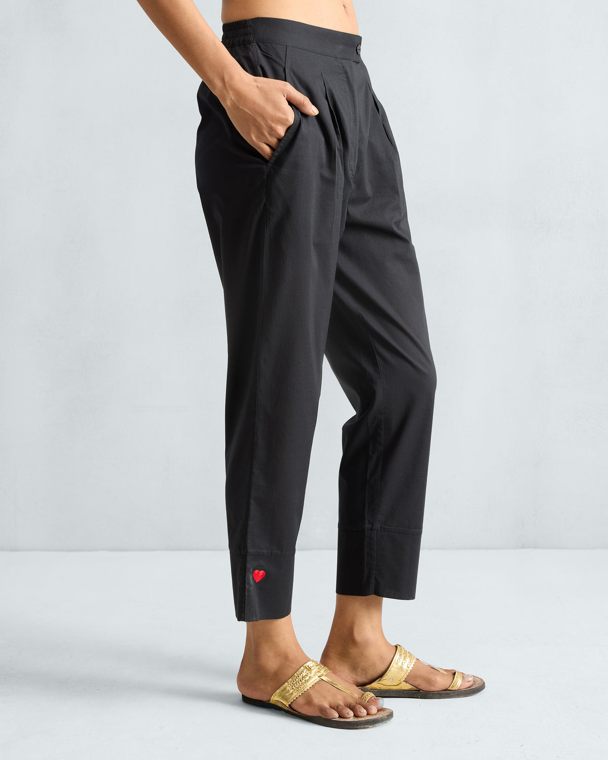 Side view of black Narrow pants with a red heart at the cropped hem.