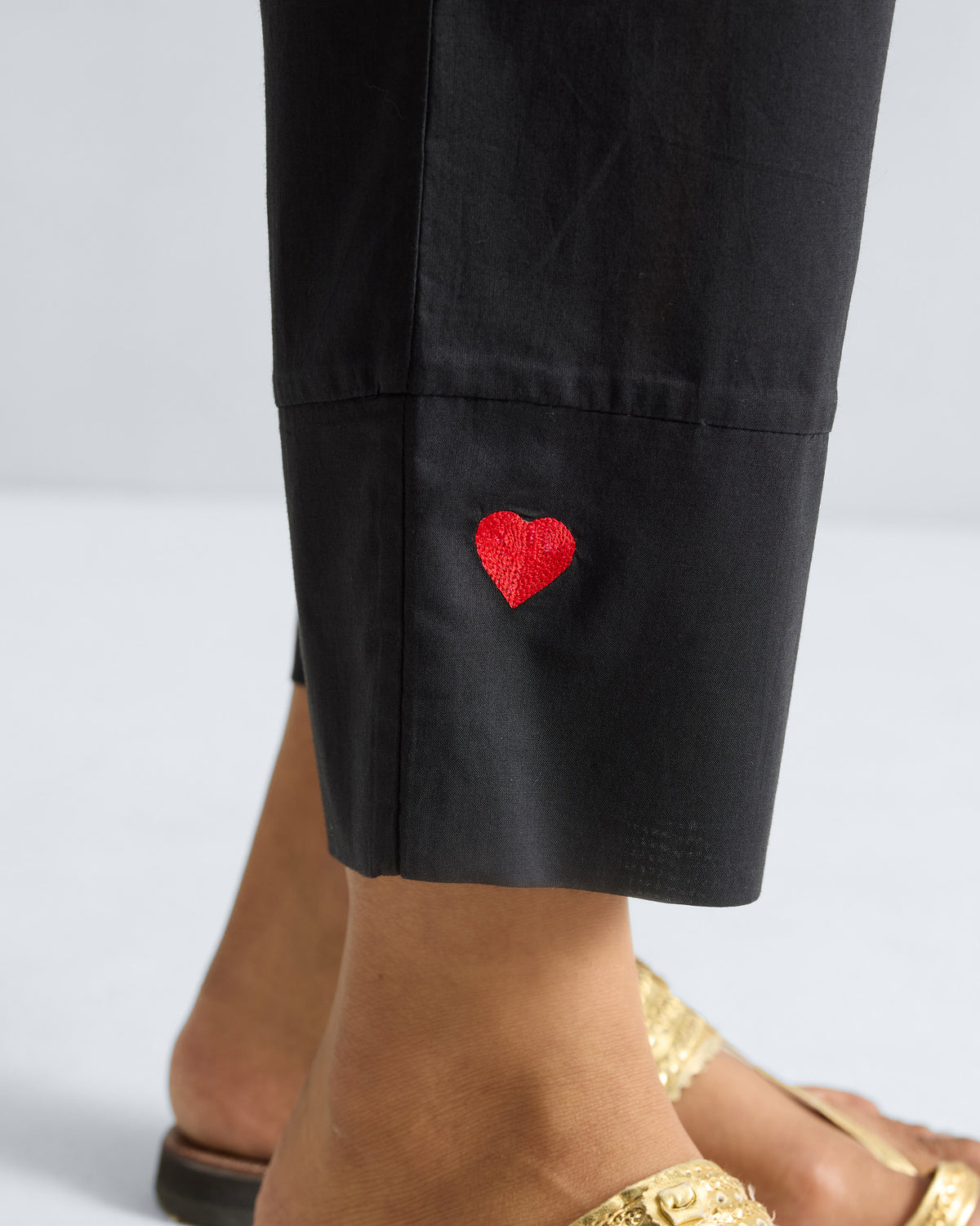 Close-up of a red embroidered heart on the cuff of black Narrow pants.
