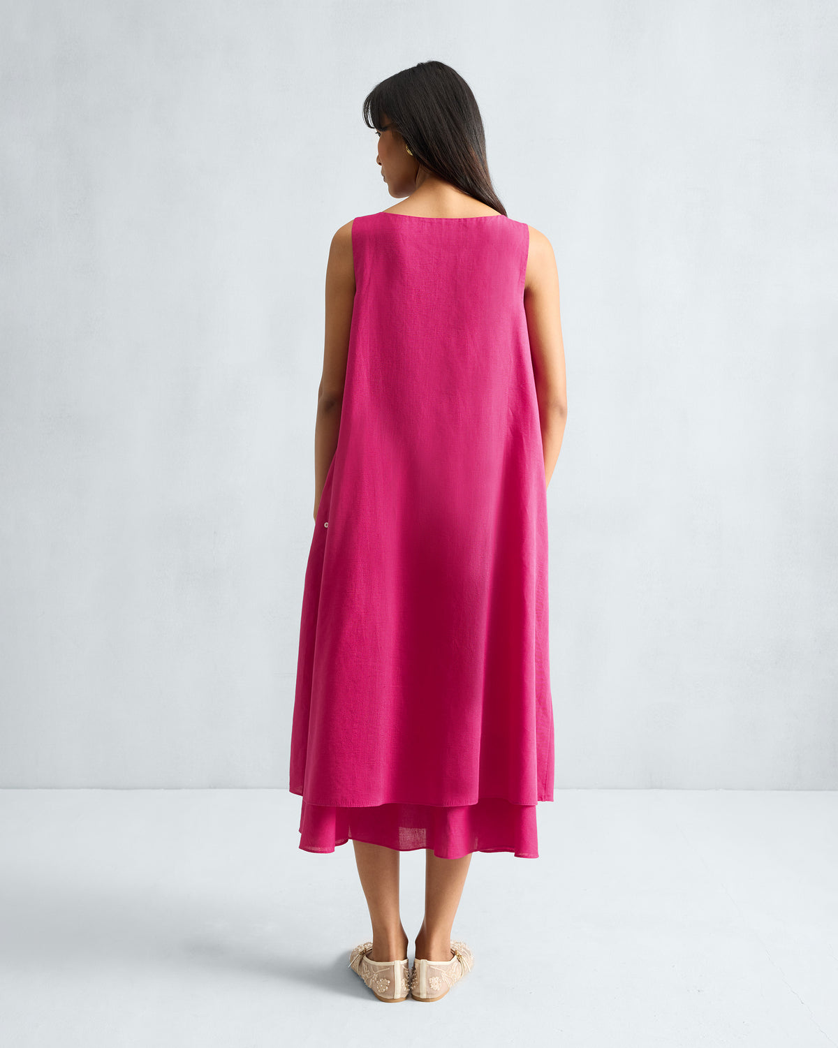Back of a fuchsia sleeveless midi dress with a layered hem.