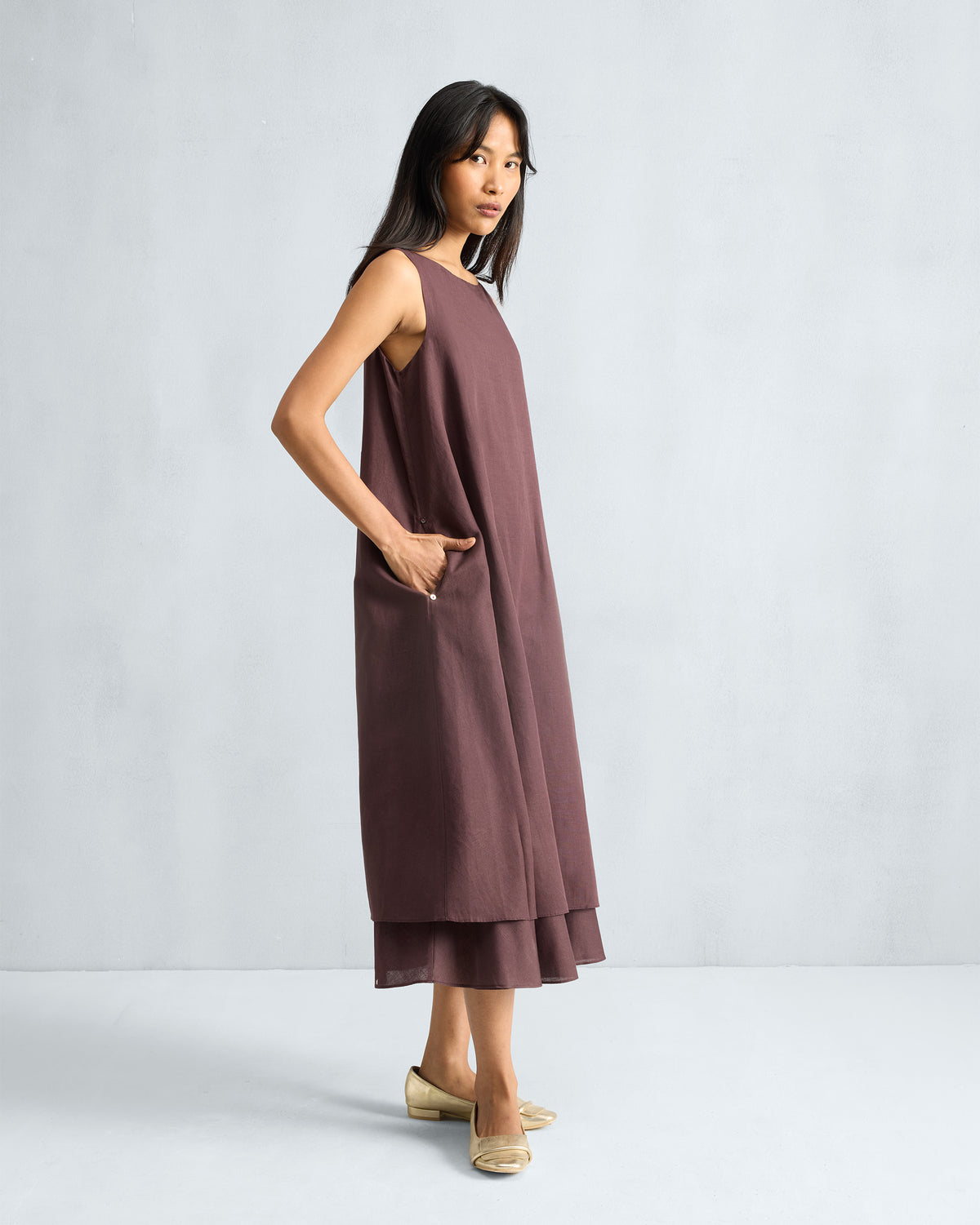 Side view of a chocolate plum Double Layer Dress with a hand in the pocket.