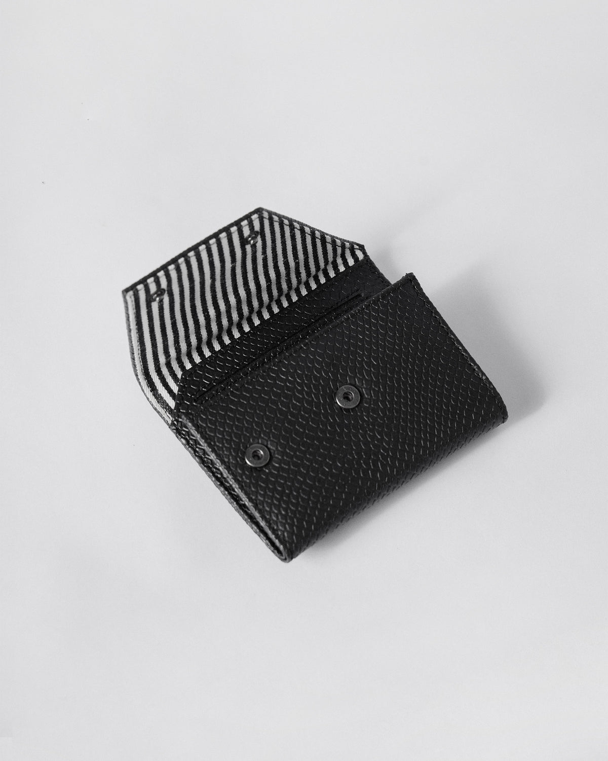 Open black wallet flap showing black-and-white striped lining and snap closures.