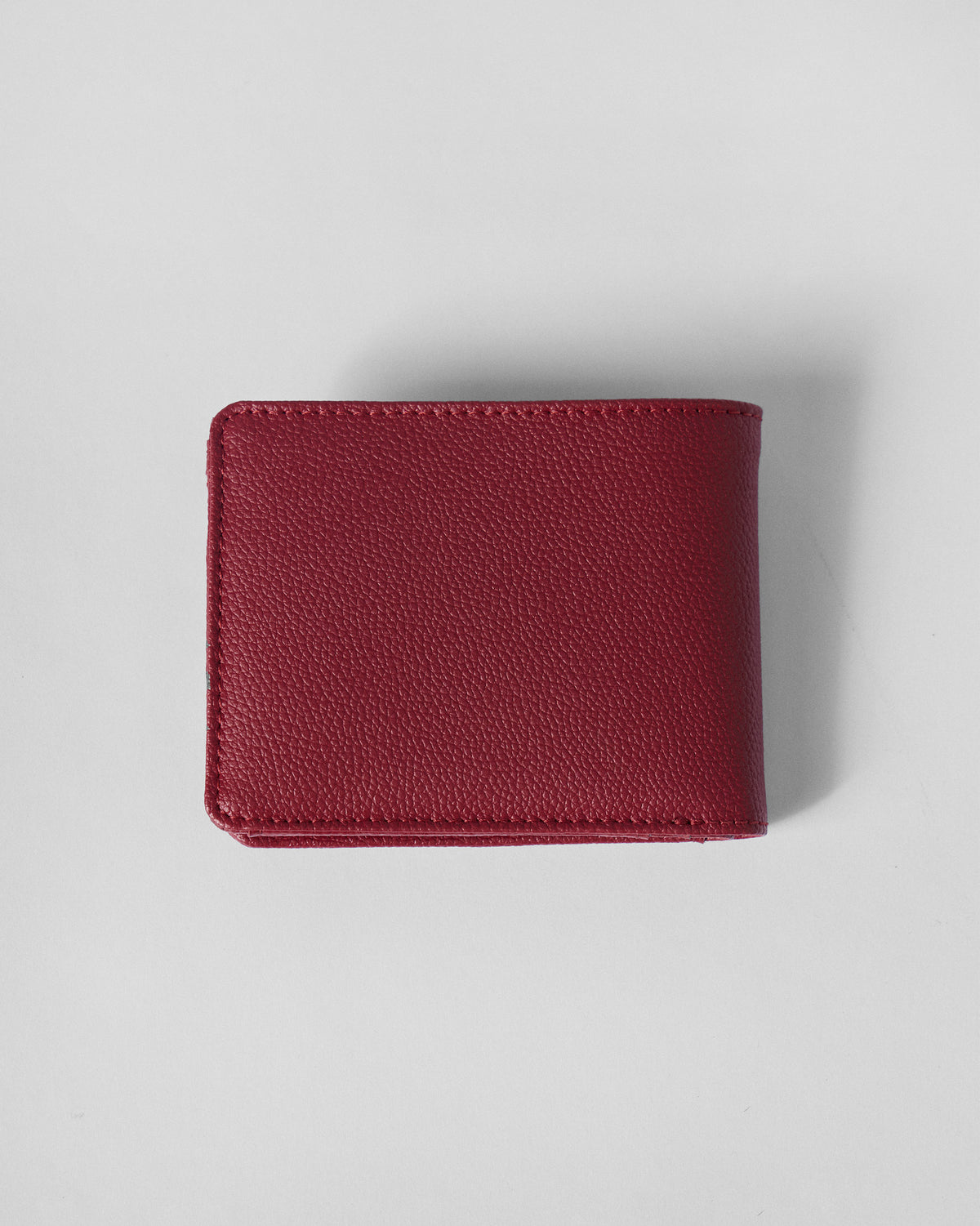 Closed red pebbled bi-fold wallet showing tonal stitching.