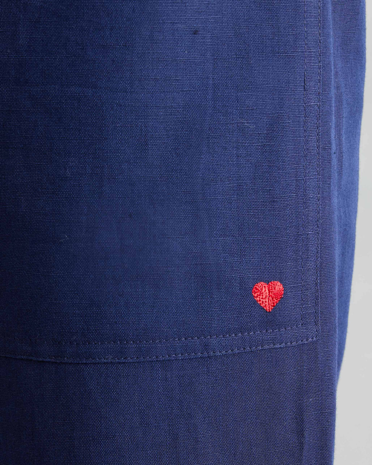 Close-up of ink blue Serene pants showing a red embroidered heart on the pocket.