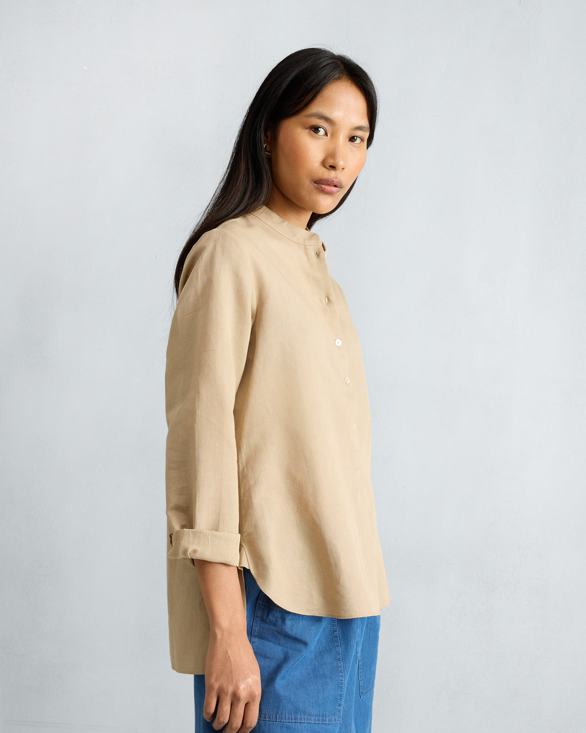 Side view of a beige mandarin collar top with a curved hem.